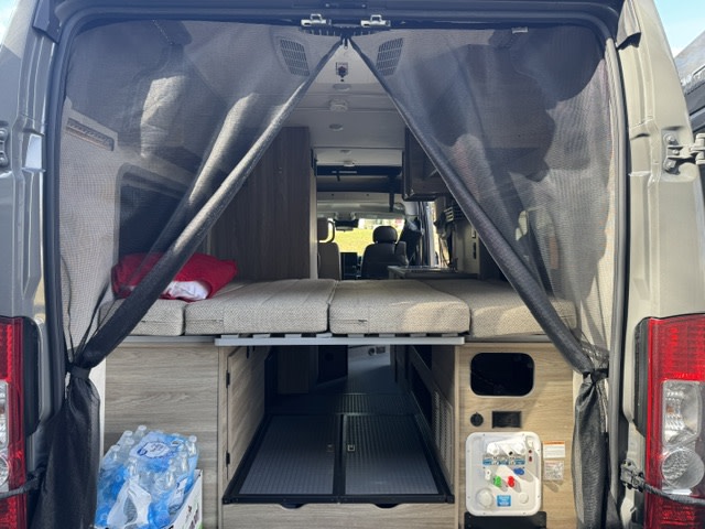 This RV rental shows its modular interior from the rear, featuring a rear screen door, bed, storage, and utility panel.. Winnebago Winnebago 2025