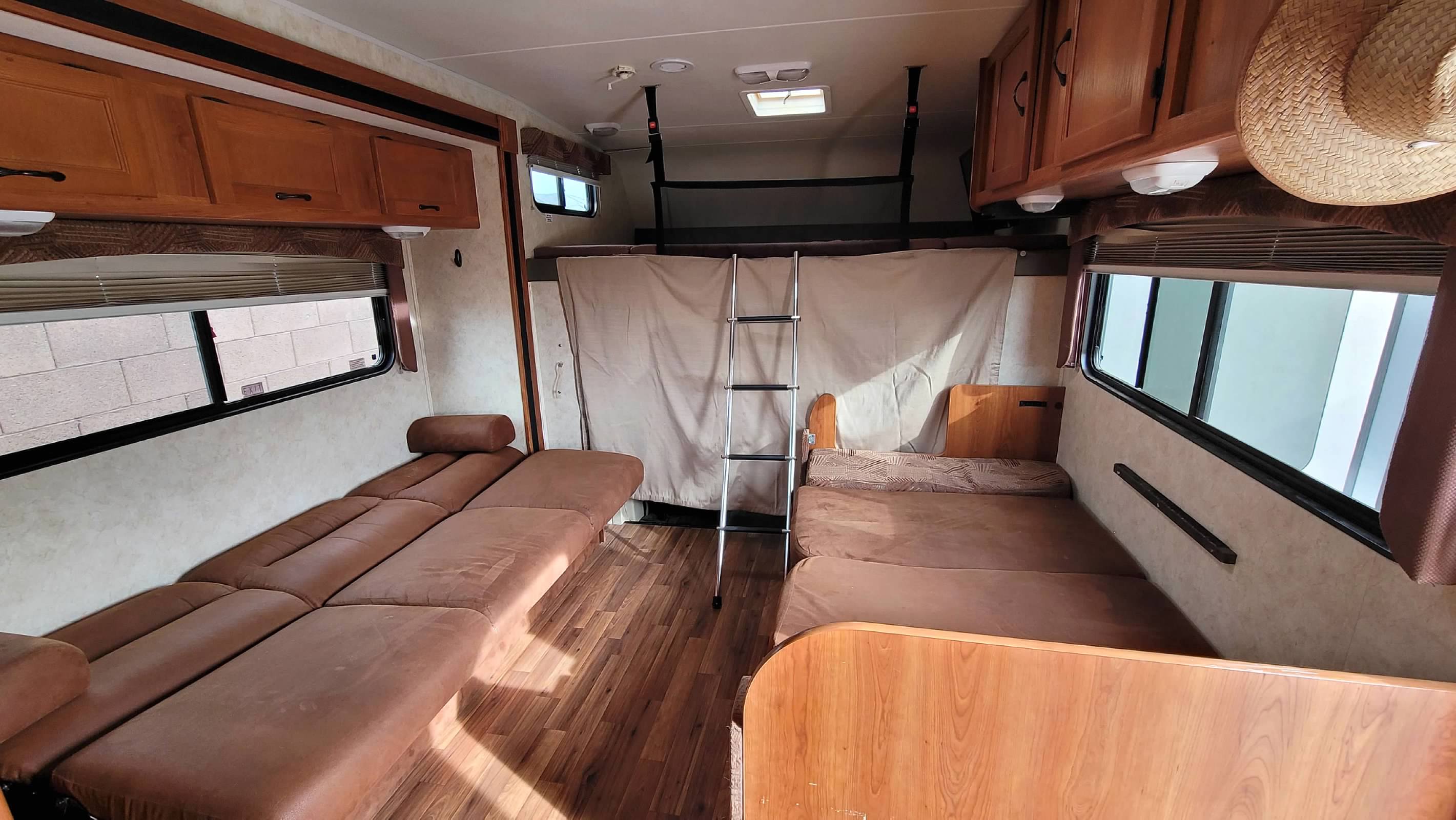 RV rental interior features brown convertible seating, multiple bunk beds, and storage cabinets, with windows on both sides.. Forest River Coachmen Freelander 2012