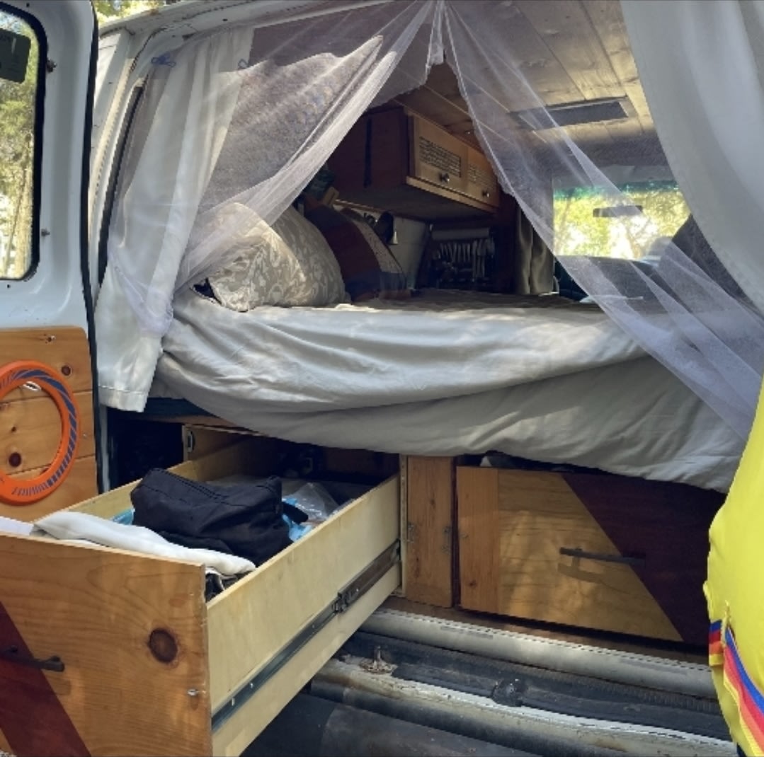 Cozy RV rental campervan interior: bed with mosquito net & pull-out wooden storage drawers. Ideal for mobile living.. Ford Econoline 2007