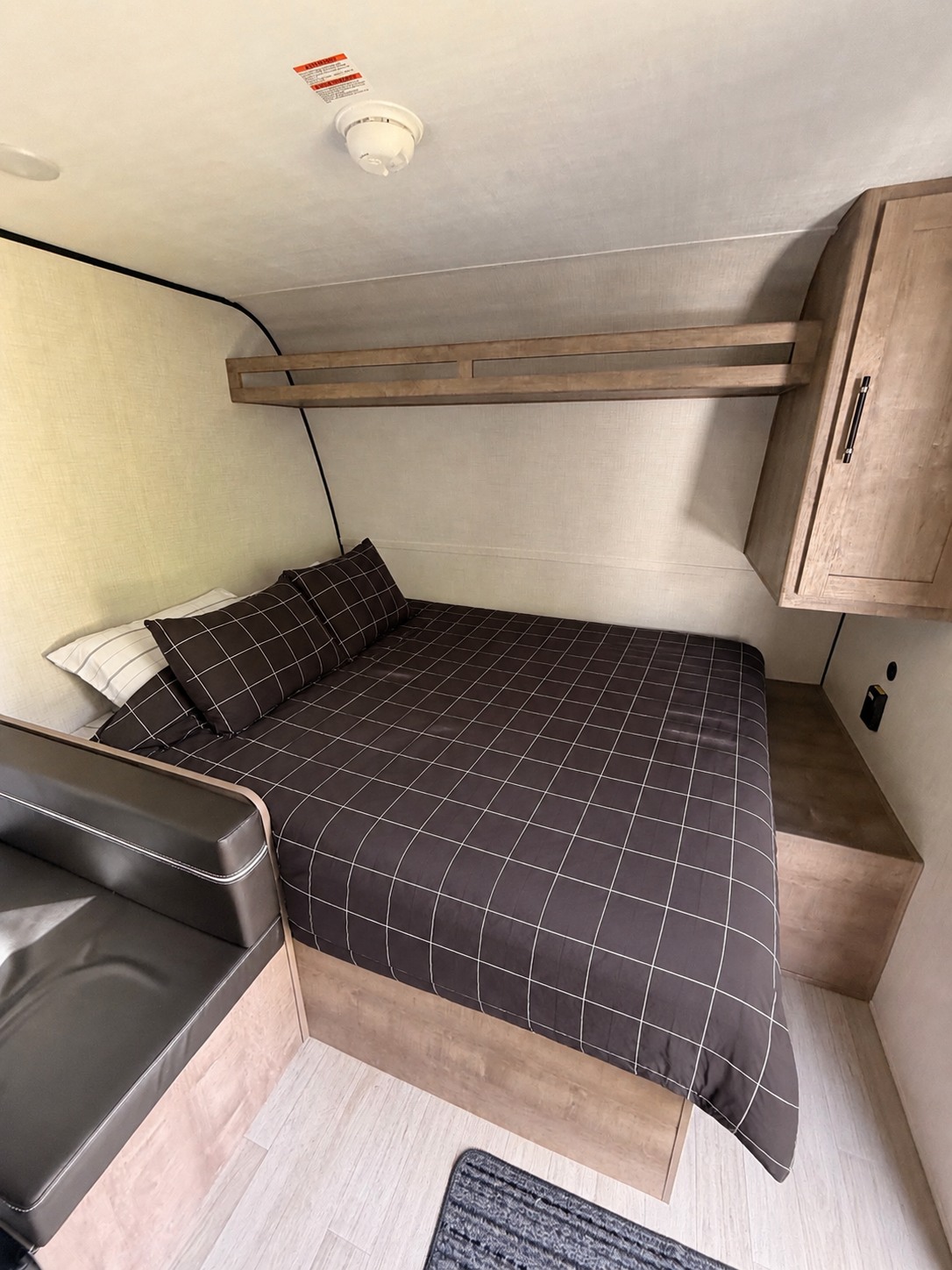 Inside this RV rental, a compact bedroom features a dark checkered queen bed, overhead shelf, and a small sofa. Functional and cozy space.. Keystone RV Springdale Mini 1610BH 2026