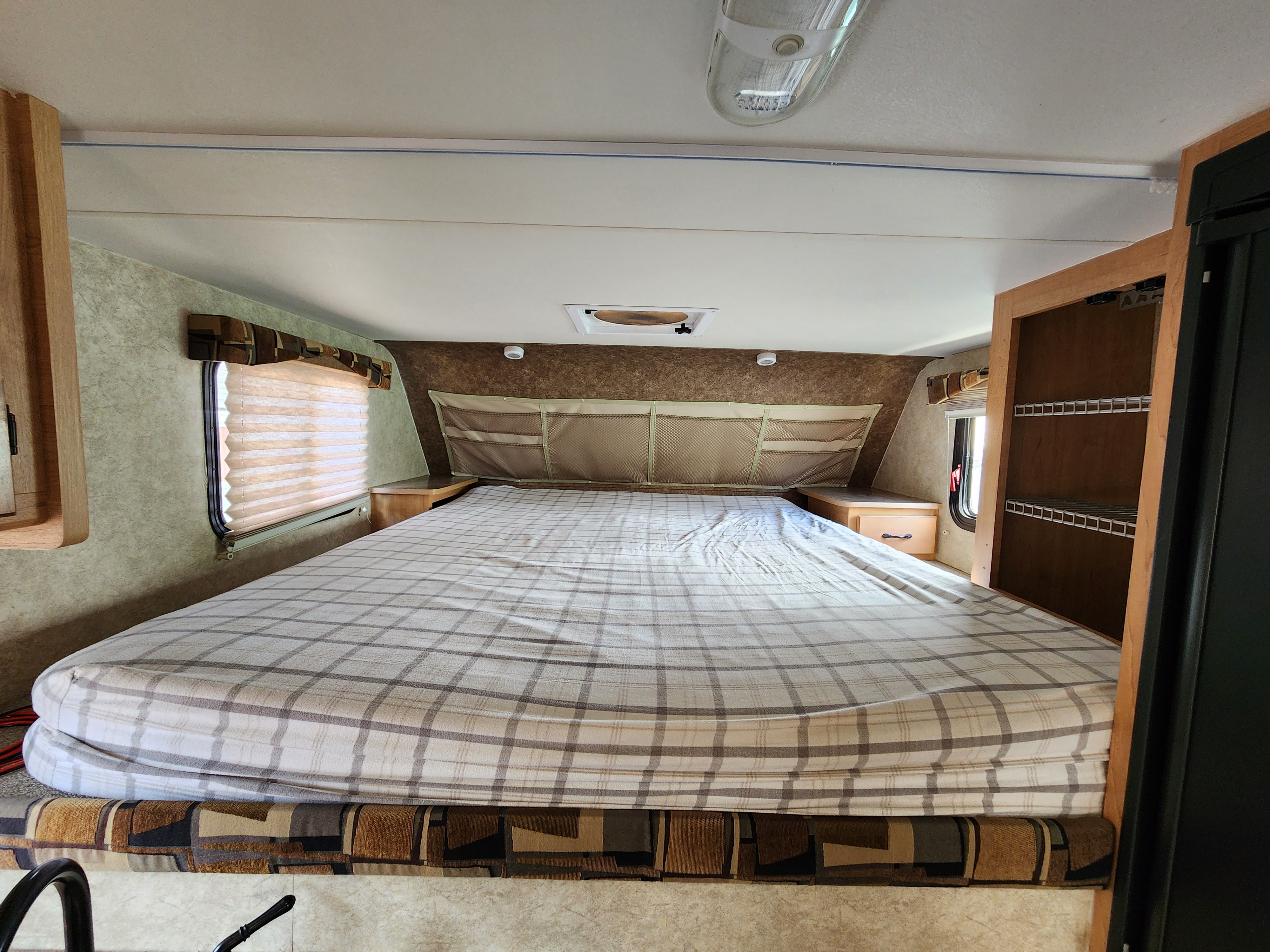 This rv rental boasts a spacious bed with plaid bedding, built-in side tables, and overhead storage, ideal for travelers.. Ford Ford F150 2018
