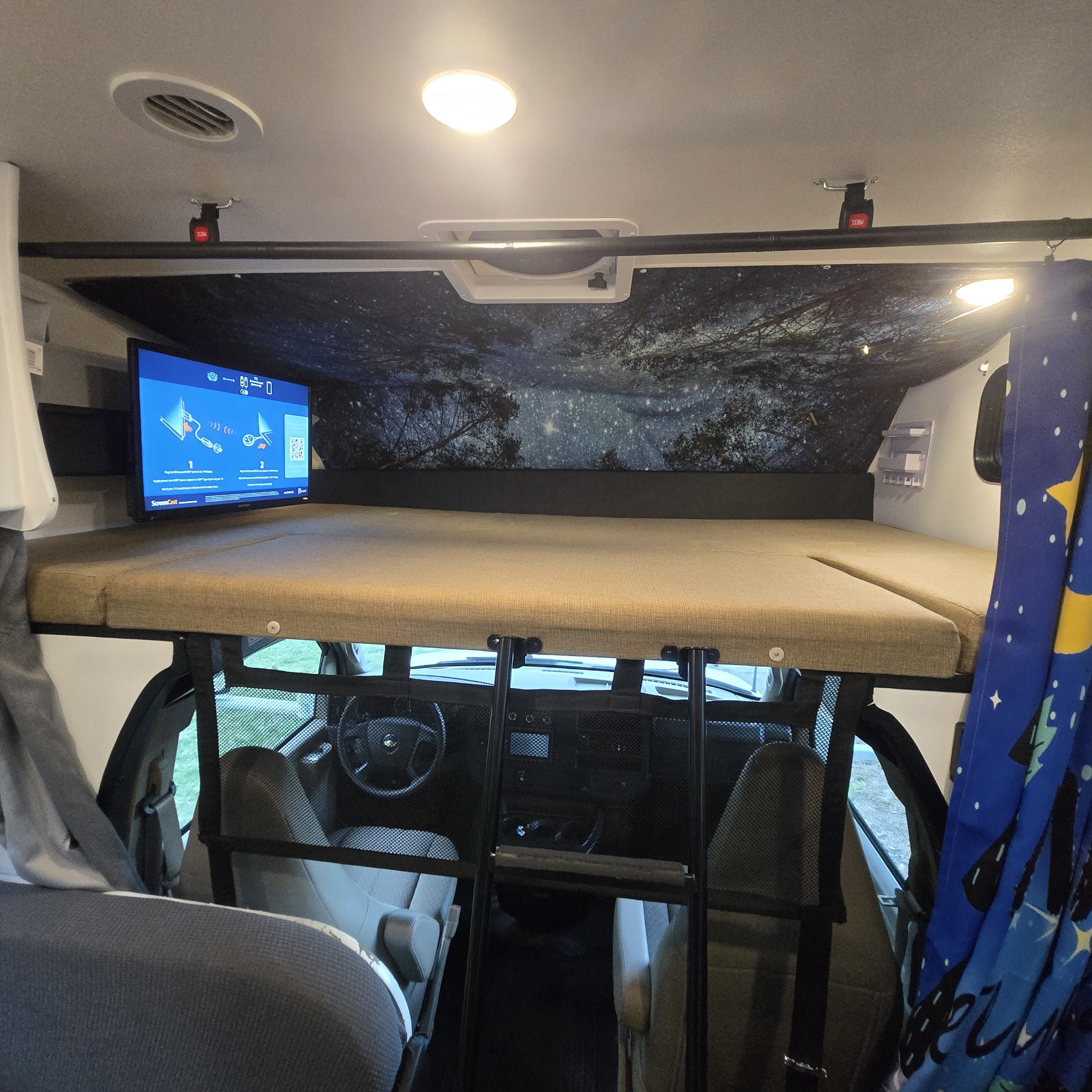 Cozy cab-over bunk in an rv rental, featuring a TV, starry ceiling, and view into the driver's cabin.. Forest River Coachmen Freelander 2017
