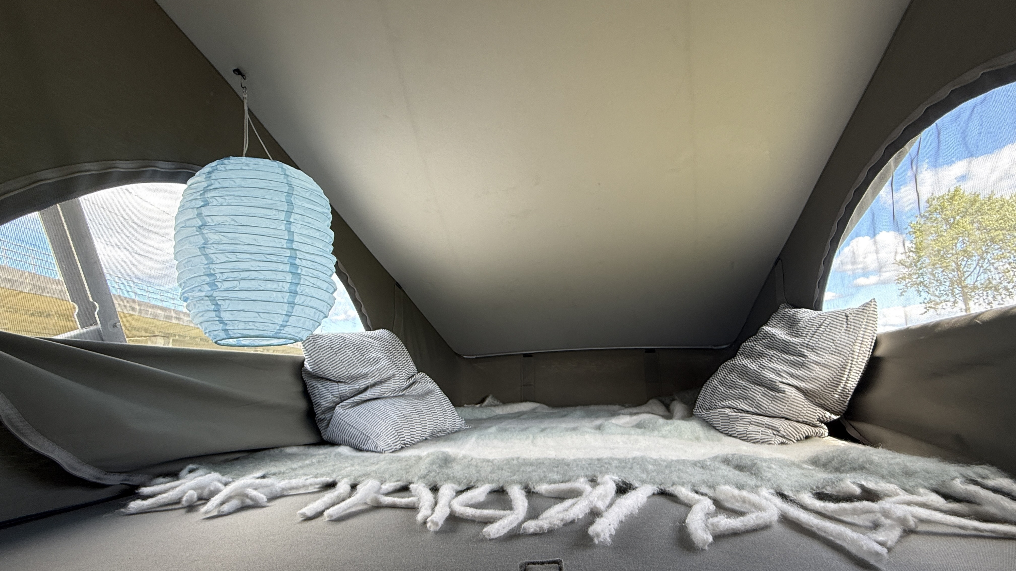 Cozy rv rental pop-top bed with pillows, blanket, & lantern. Windows show sky & trees, creating a serene space.. Volkswagen T6 2018