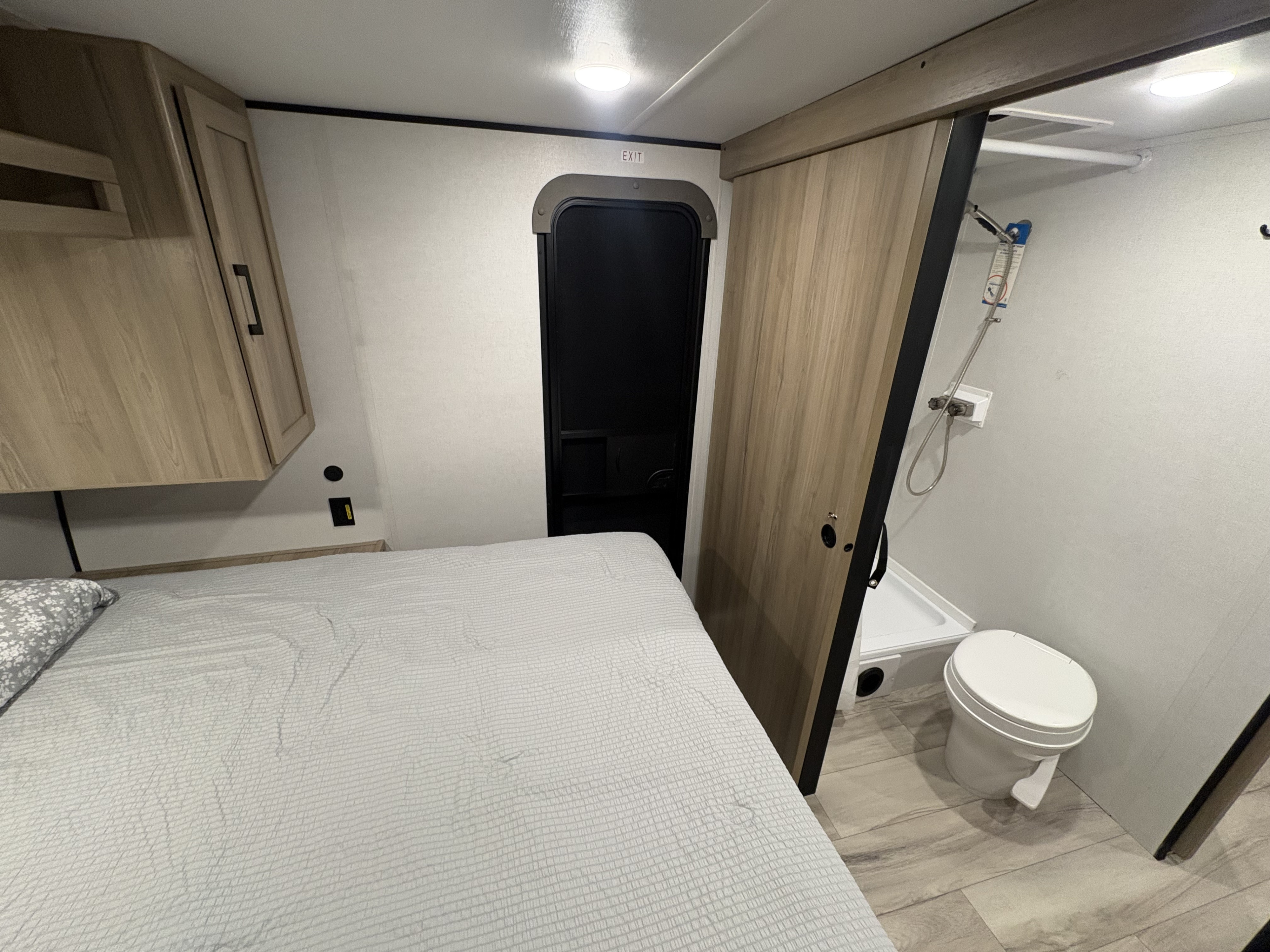 Inside an RV rental: a compact bedroom with a bed, overhead cabinets, and an adjacent bathroom with a toilet and shower.. Keystone RV Other 2026