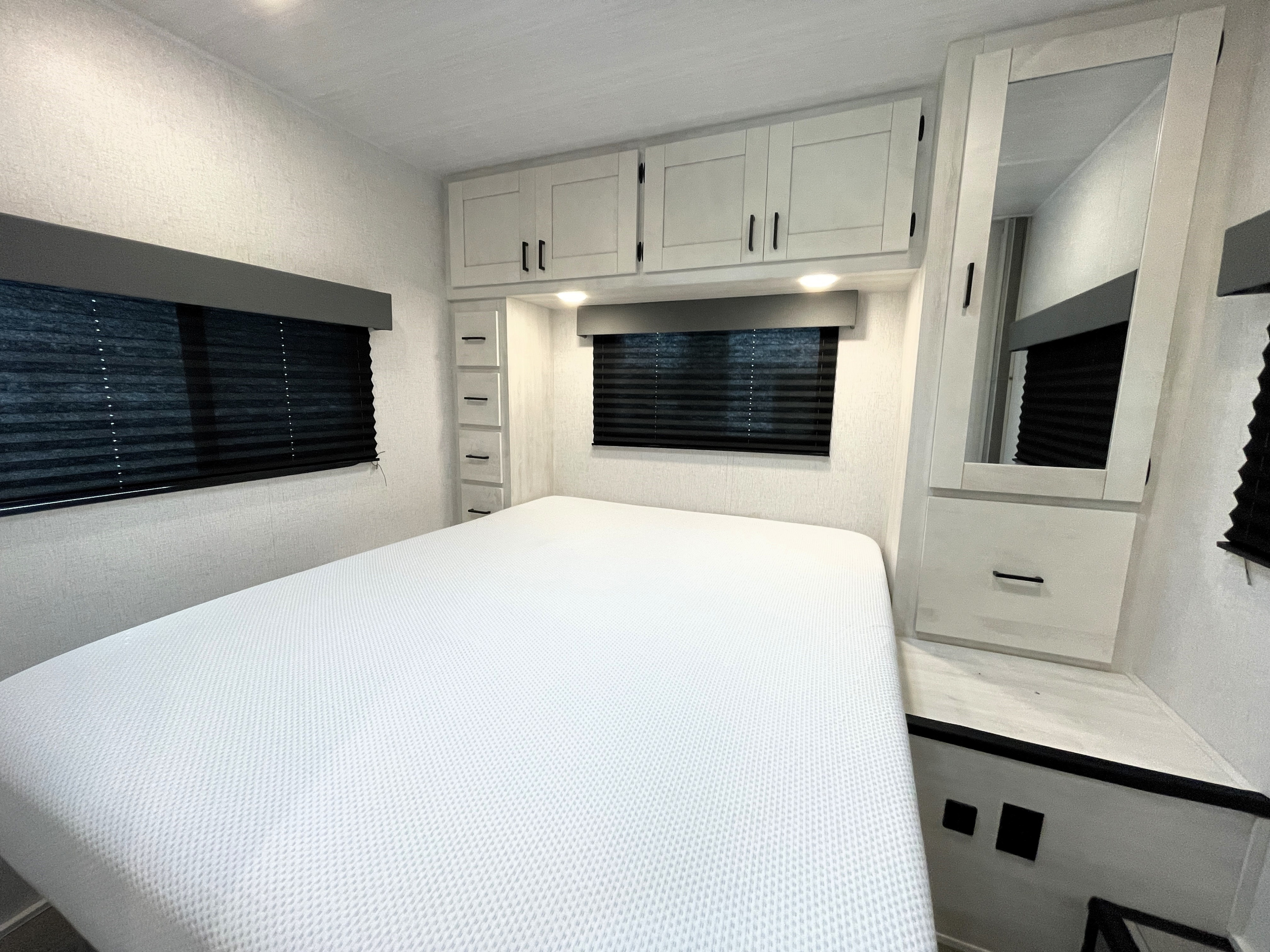 Spacious and modern RV rental bedroom featuring a large bed, overhead cabinets, side storage with a mirror, and blackout blinds.. Entrada Entrada Motorhome 2022