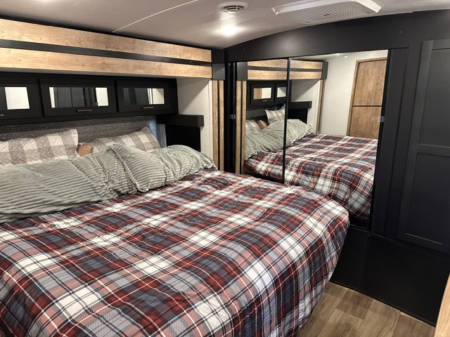 Cozy RV rental bedroom with plaid bedding, mirrored closet, and overhead storage, perfect for comfortable travel.. Keystone RV Outback 2023