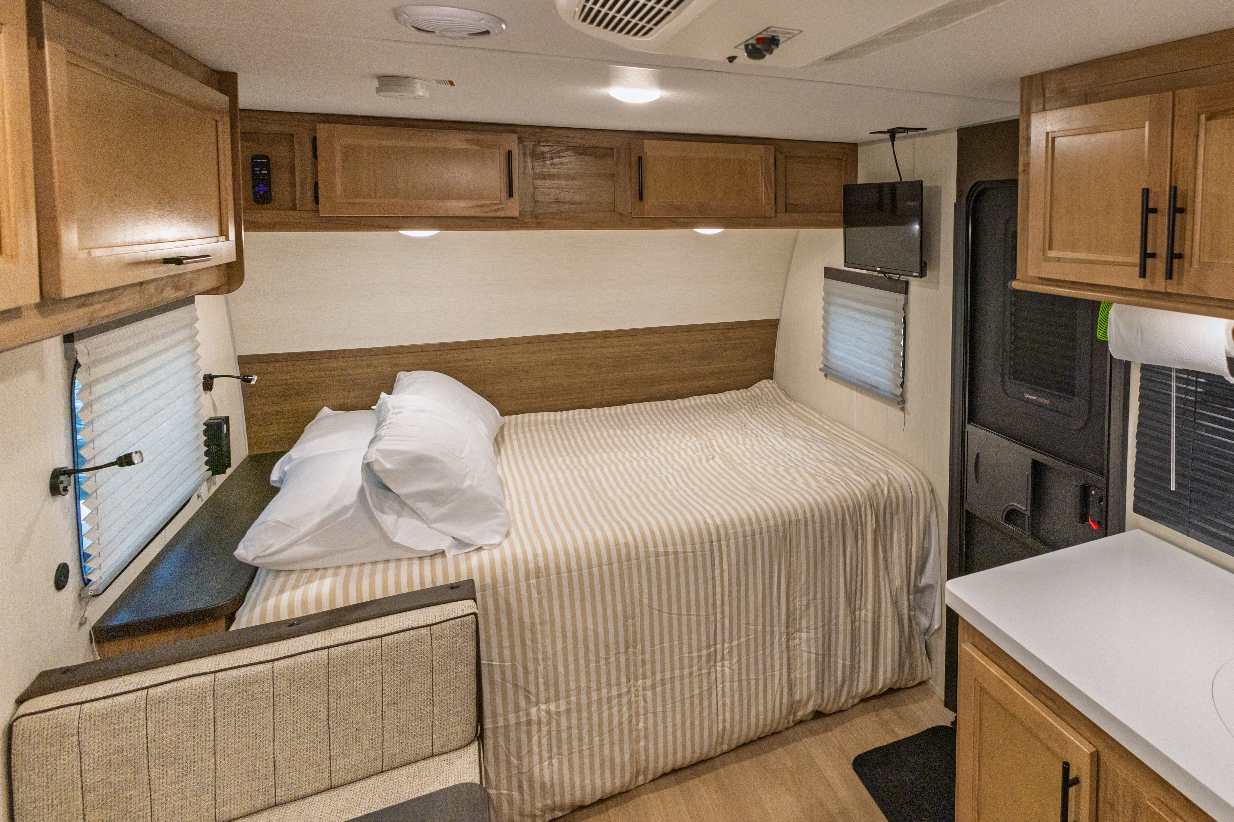 Inside an RV rental, this compact sleeping area features a cozy bed, overhead cabinets, TV, and nearby seating.. Forest River Cherokee Wolf Pup Black Label 2025