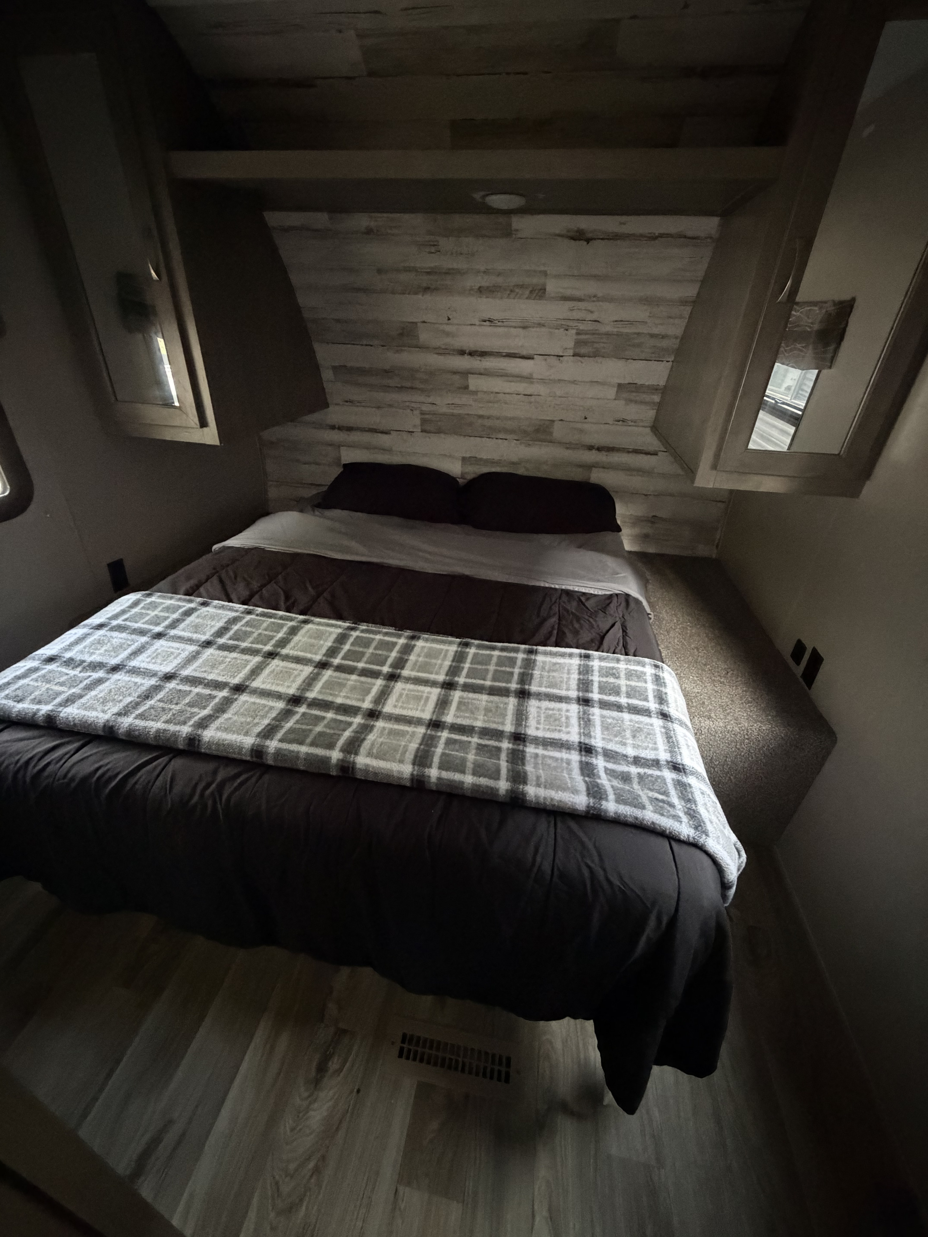 RV rental: A cozy bedroom with a bed, dark bedding, and a plaid blanket. Features plank walls, built-in cabinets, and wood-style flooring.. Forest River Palomino Puma XLE 2023