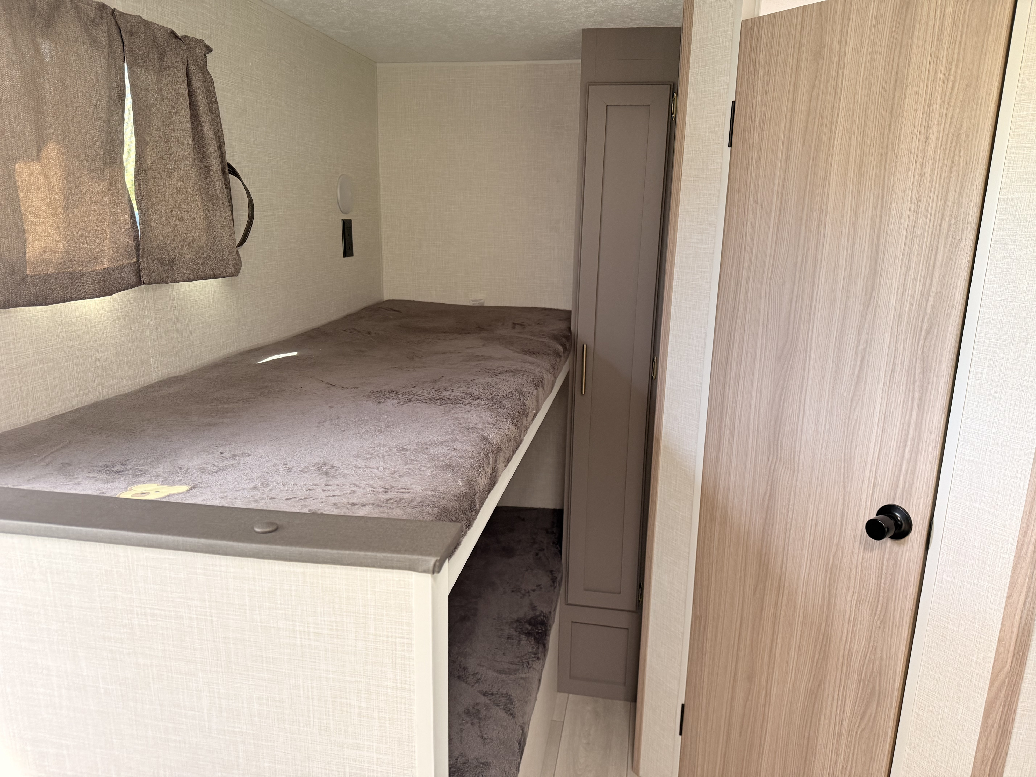 RV rental bunk beds: a compact sleeping area with textured walls, a grey plush mattress, and a nearby storage cabinet.. KZ Sportsmen Classic 2025