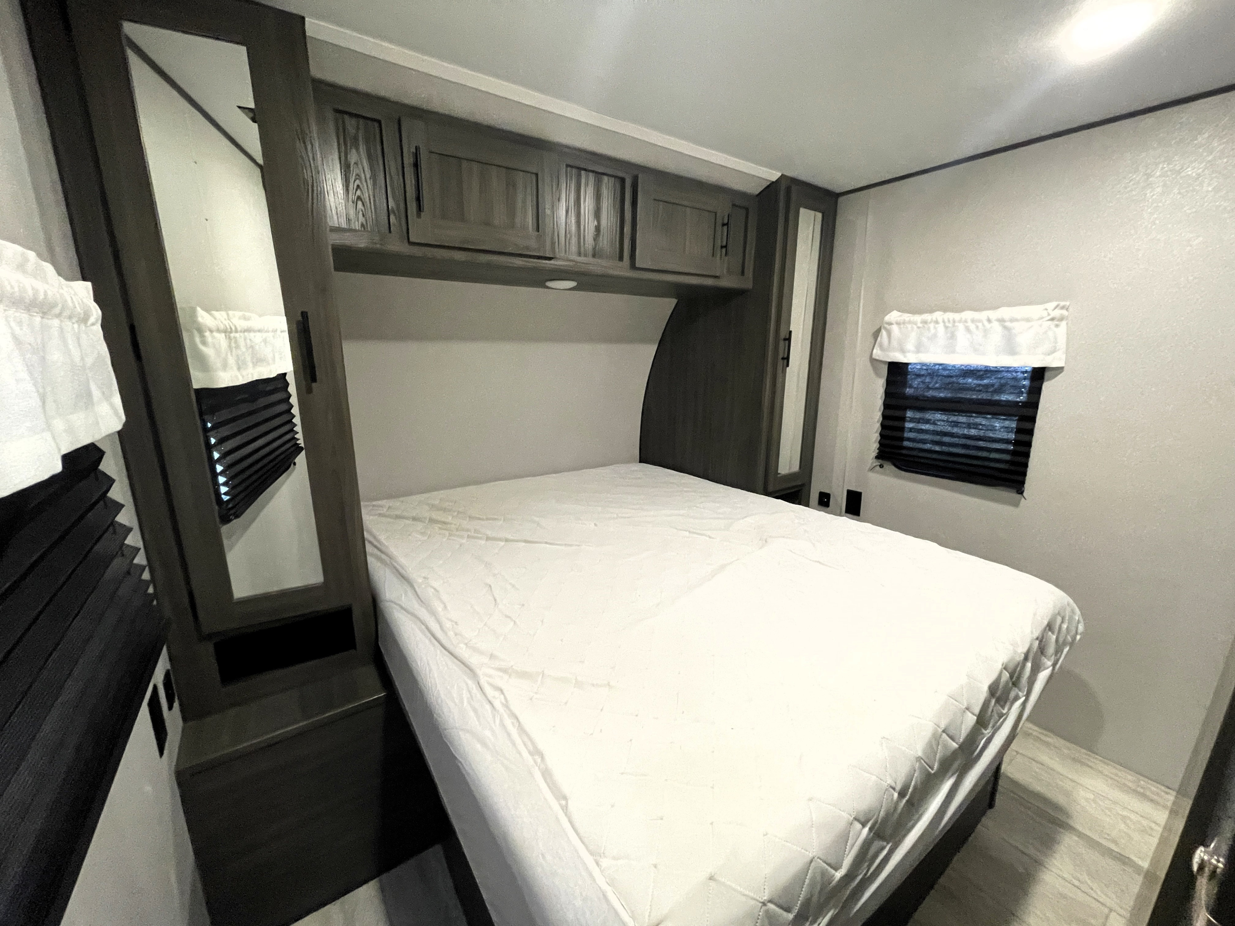 Clean RV rental bedroom with a large bed, overhead storage, mirrored wardrobes, and a window with privacy blinds.. Shasta 26DB 2021