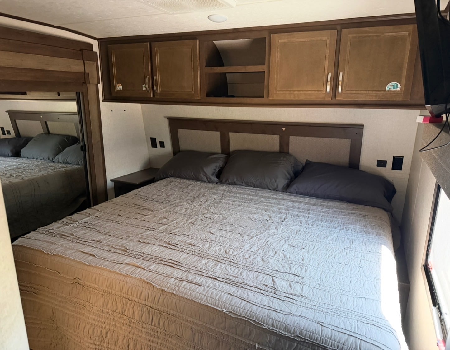 Cozy RV rental bedroom featuring a large bed with quilted bedding, overhead cabinets, and a full-length mirror.. Highland Ridge RV Open Range 2020