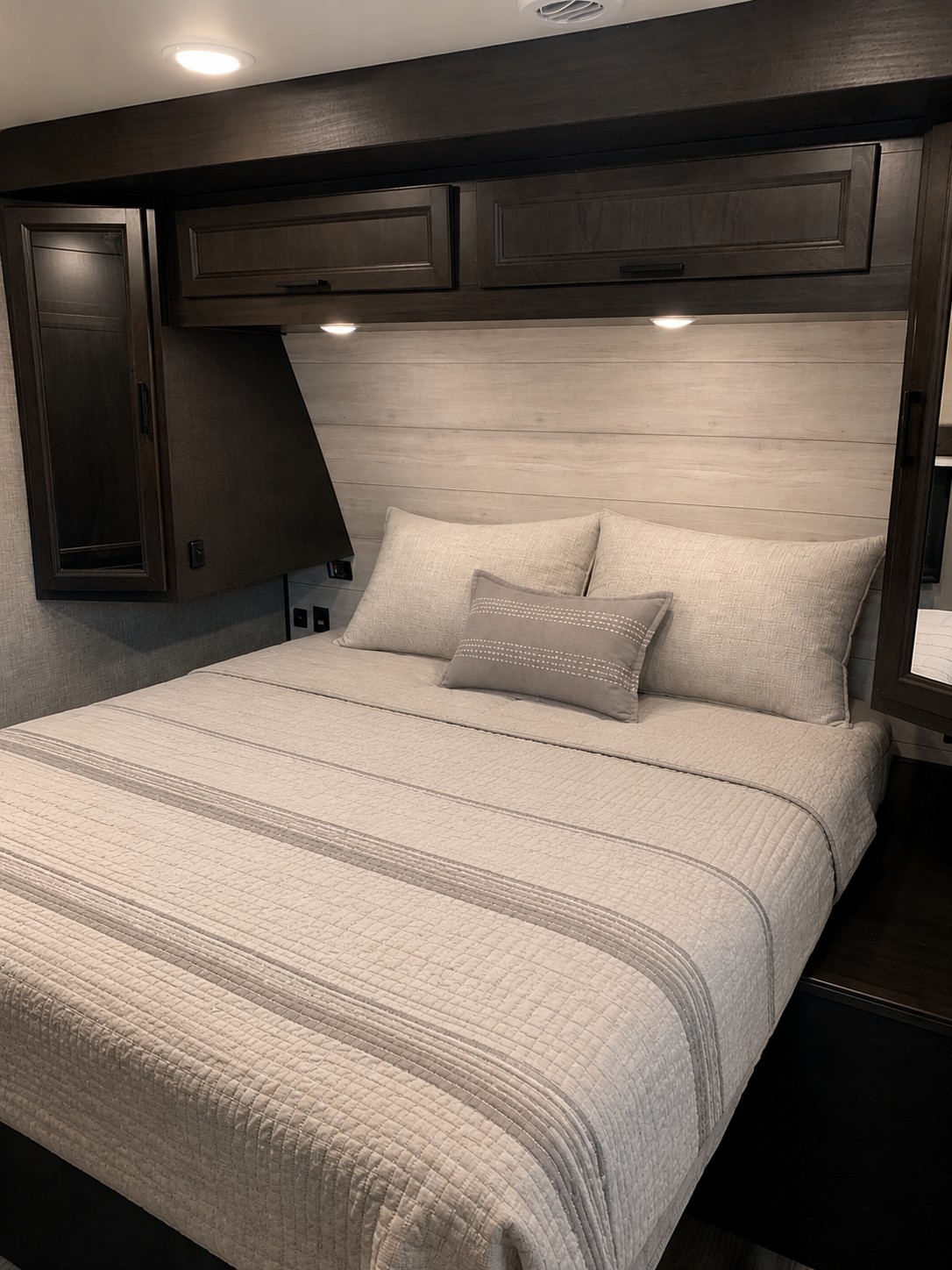 Relaxing RV rental bedroom with light wood paneling, dark overhead cabinets, reading lights, and a comfy bed with striped quilt.. Jayco Eagle HT 2022