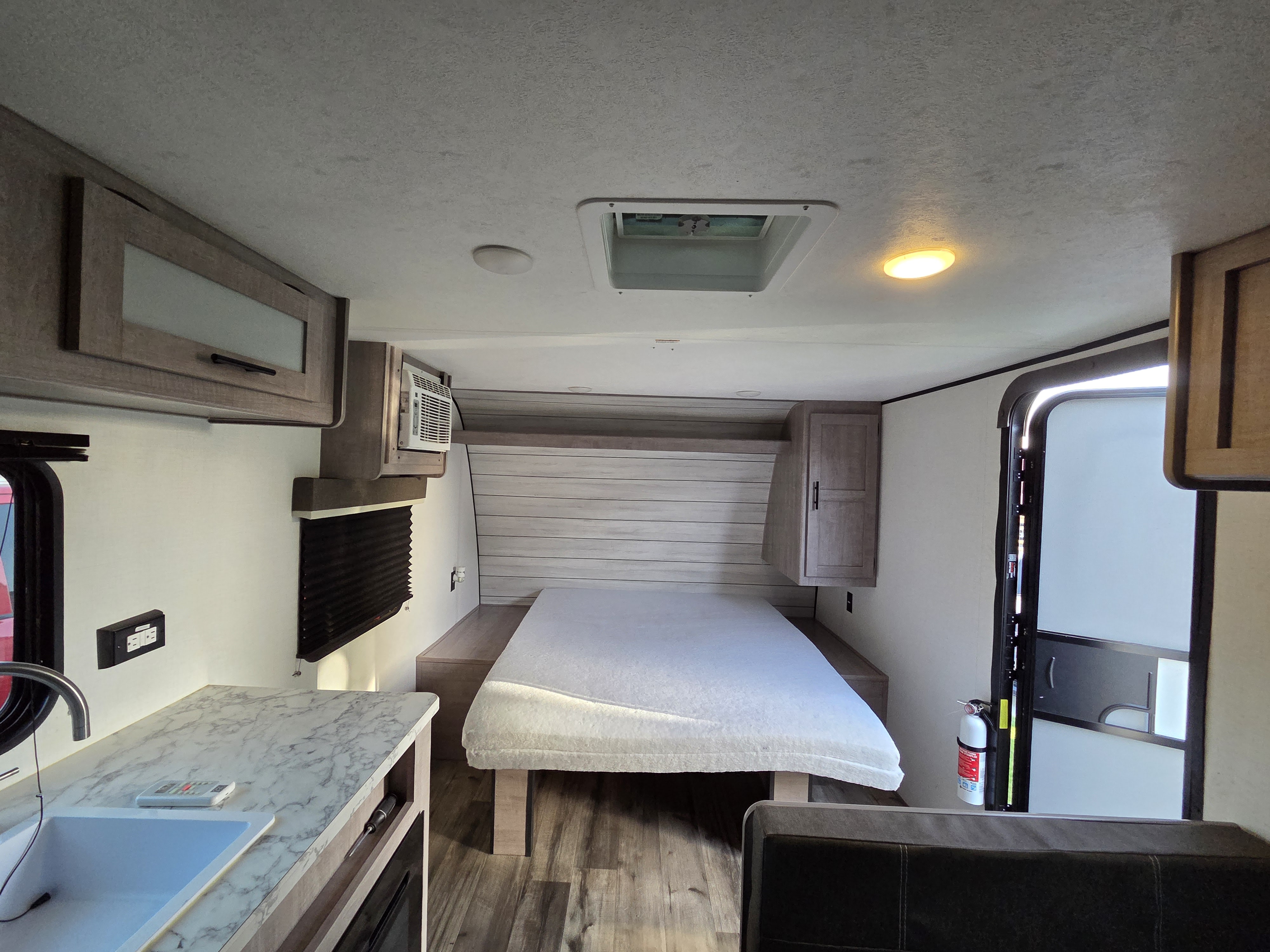 Spacious RV rental interior featuring a cozy bed, compact kitchen area with sink, overhead cabinets, and a convenient exit door.. Dutchmen Coleman 2024