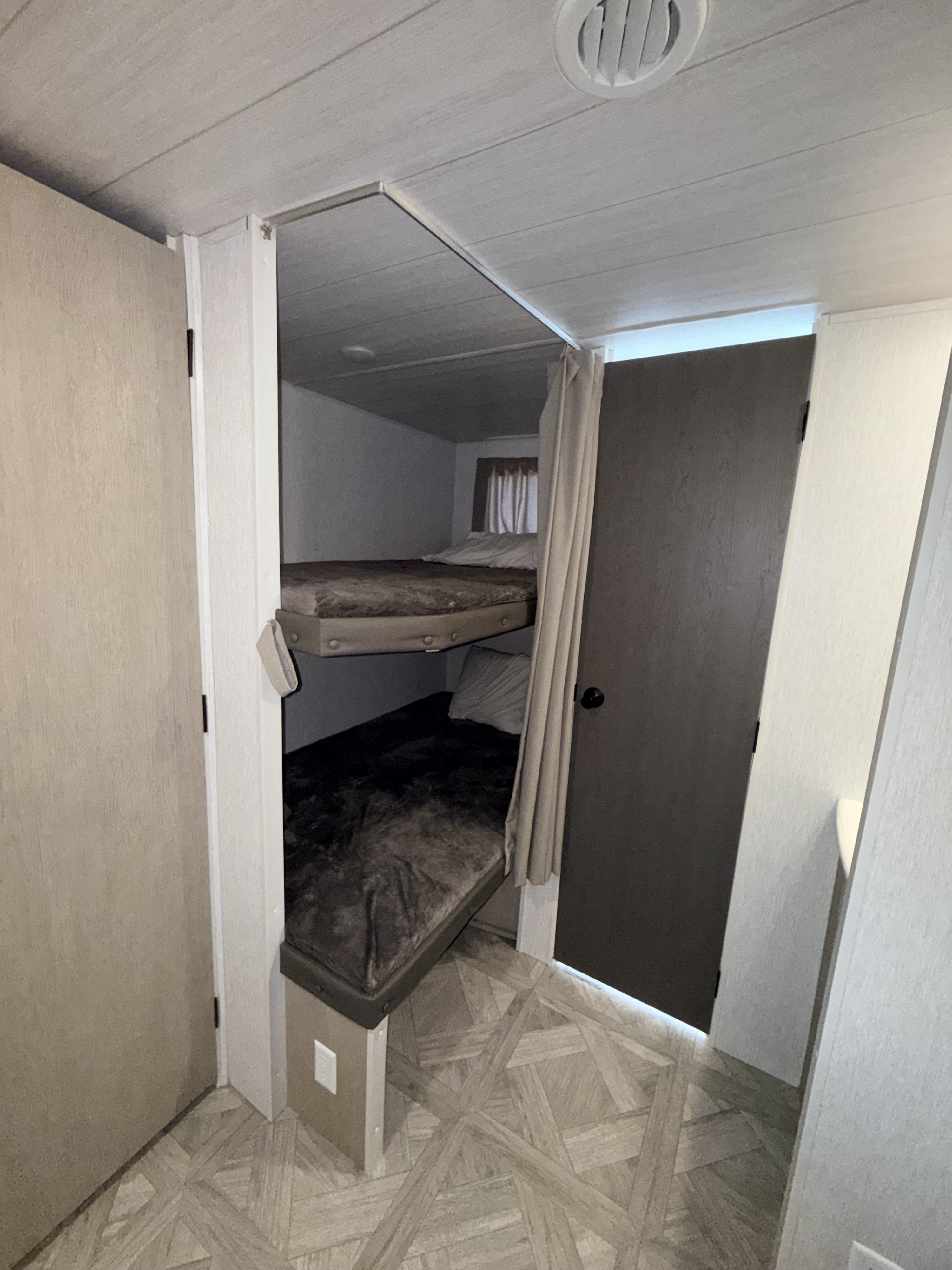 Inside an RV rental: two compact bunk beds with soft bedding and a privacy curtain, providing a cozy sleeping area in a small space.. Forest River Wildwood 2023