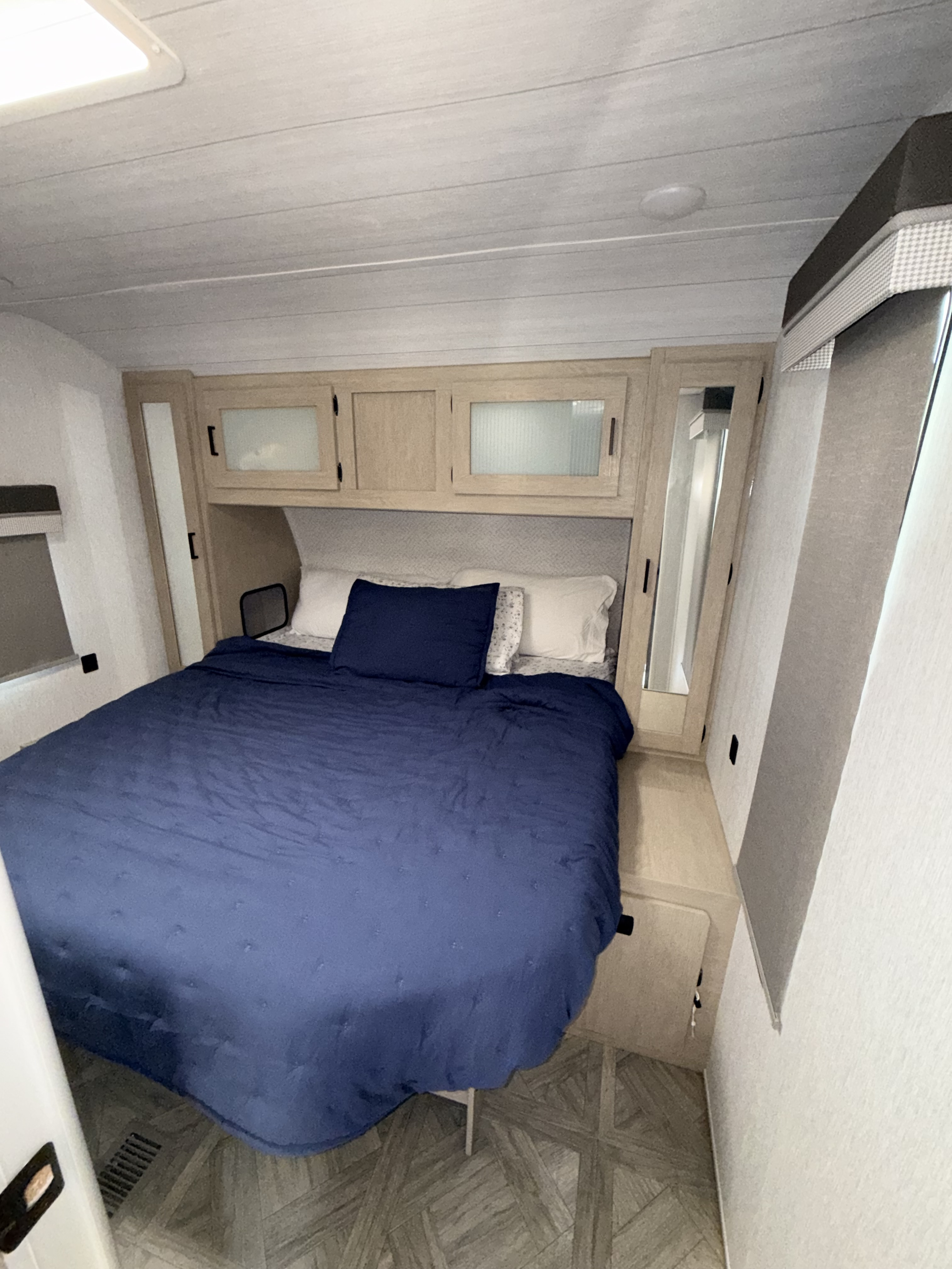 RV rental bedroom interior: compact space with blue bed, light wood cabinets, and mirrored wardrobes for cozy travels.. Forest River Wildwood 2023