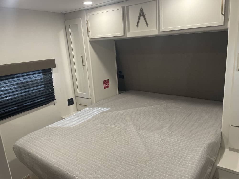 Bright RV rental bedroom: bed, window, and modern cabinets (one with an 'A' handle) offer comfort for your journeys.. Grand Design Transcend 2026