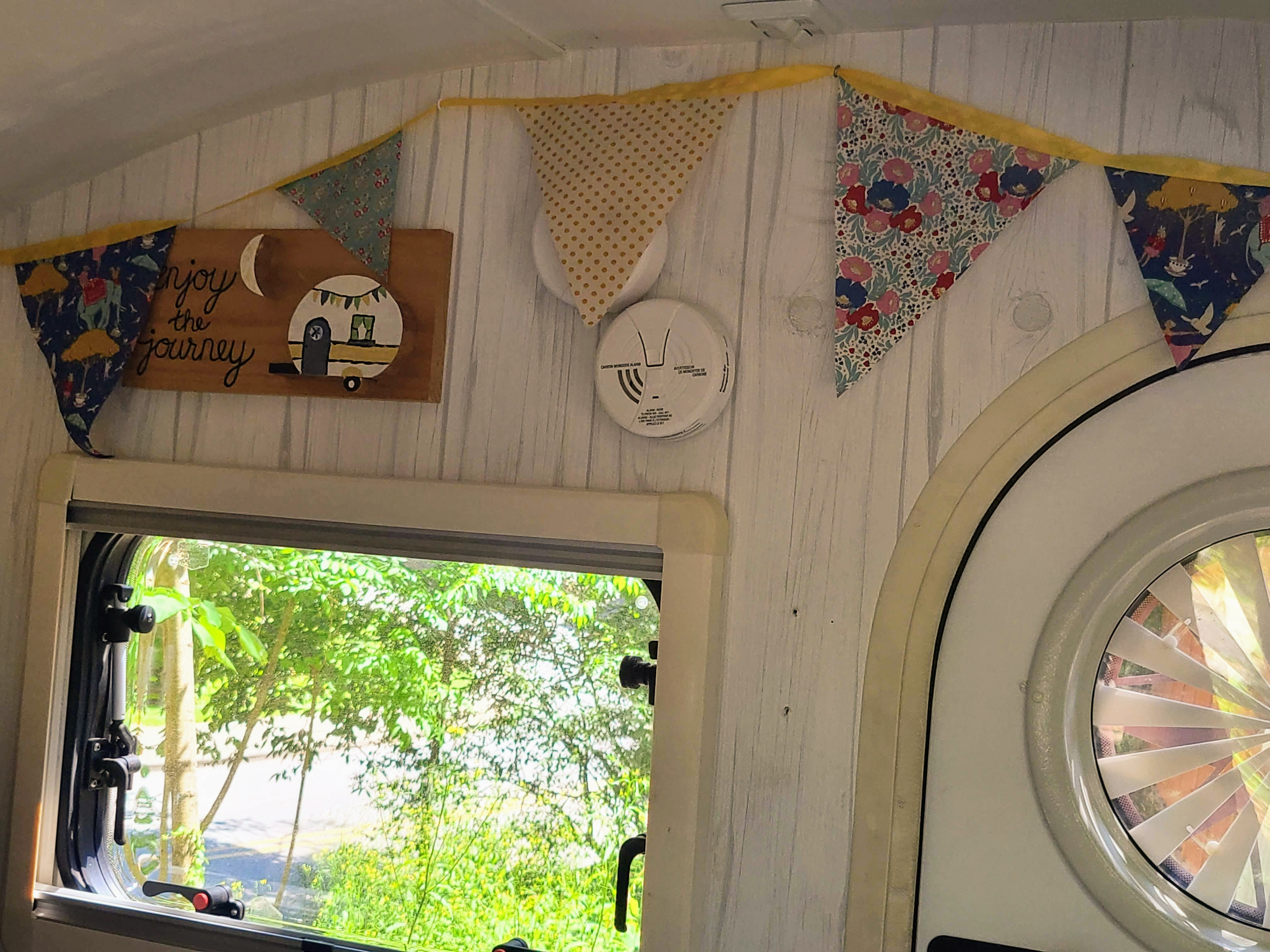 Cozy RV rental interior with decorative bunting, "enjoy the journey" sign, and window view of nature.. nuCamp T@G 2019