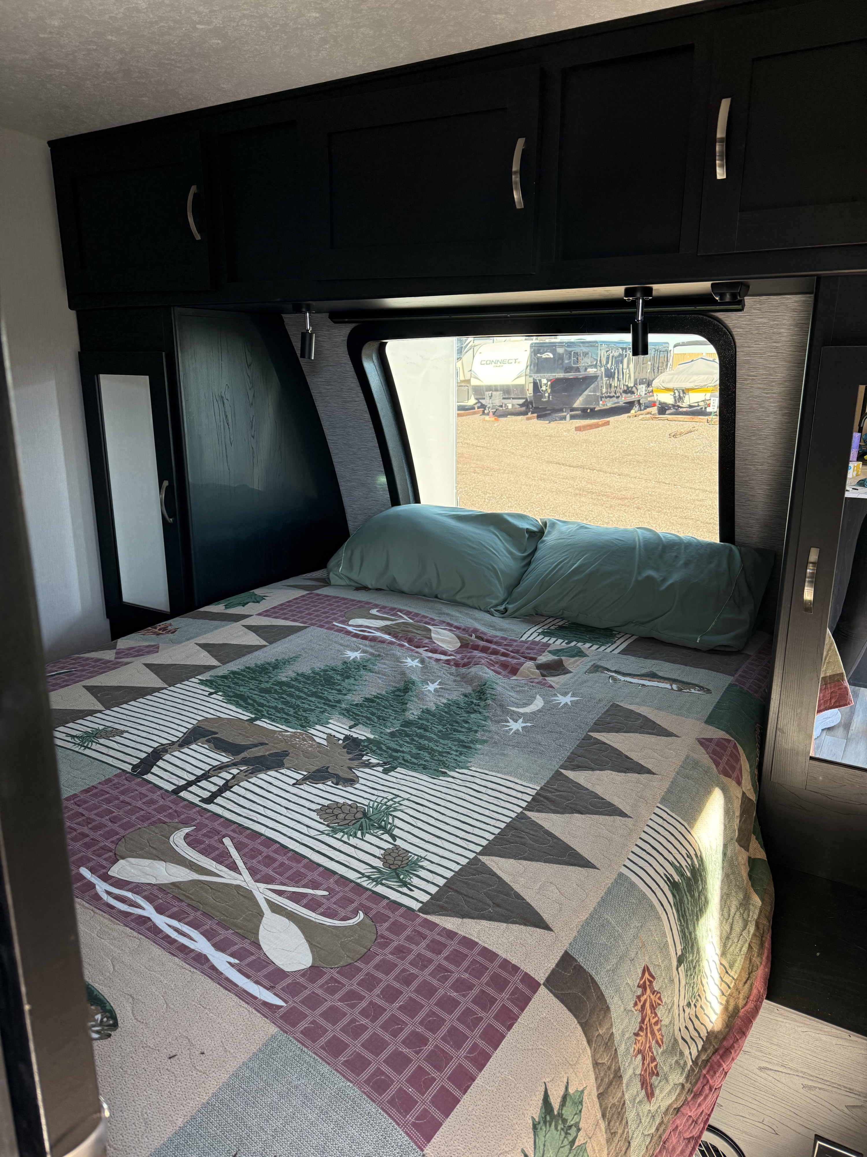 Comfortable RV rental bedroom featuring a wilderness-patterned quilt, overhead storage, and a window view of other RVs.. Coachmen Freedom Express 257BHS 2022