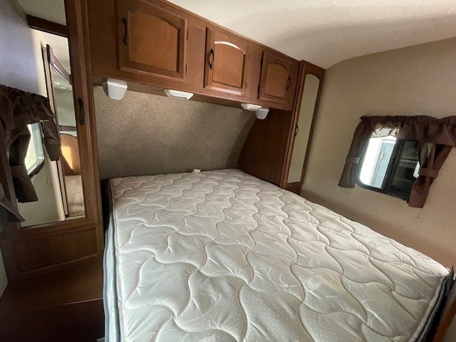 RV rental bedroom: cozy space with a comfy bed, overhead storage, & window with curtains, ideal for travel.. Coachmen Freedom Express 2015