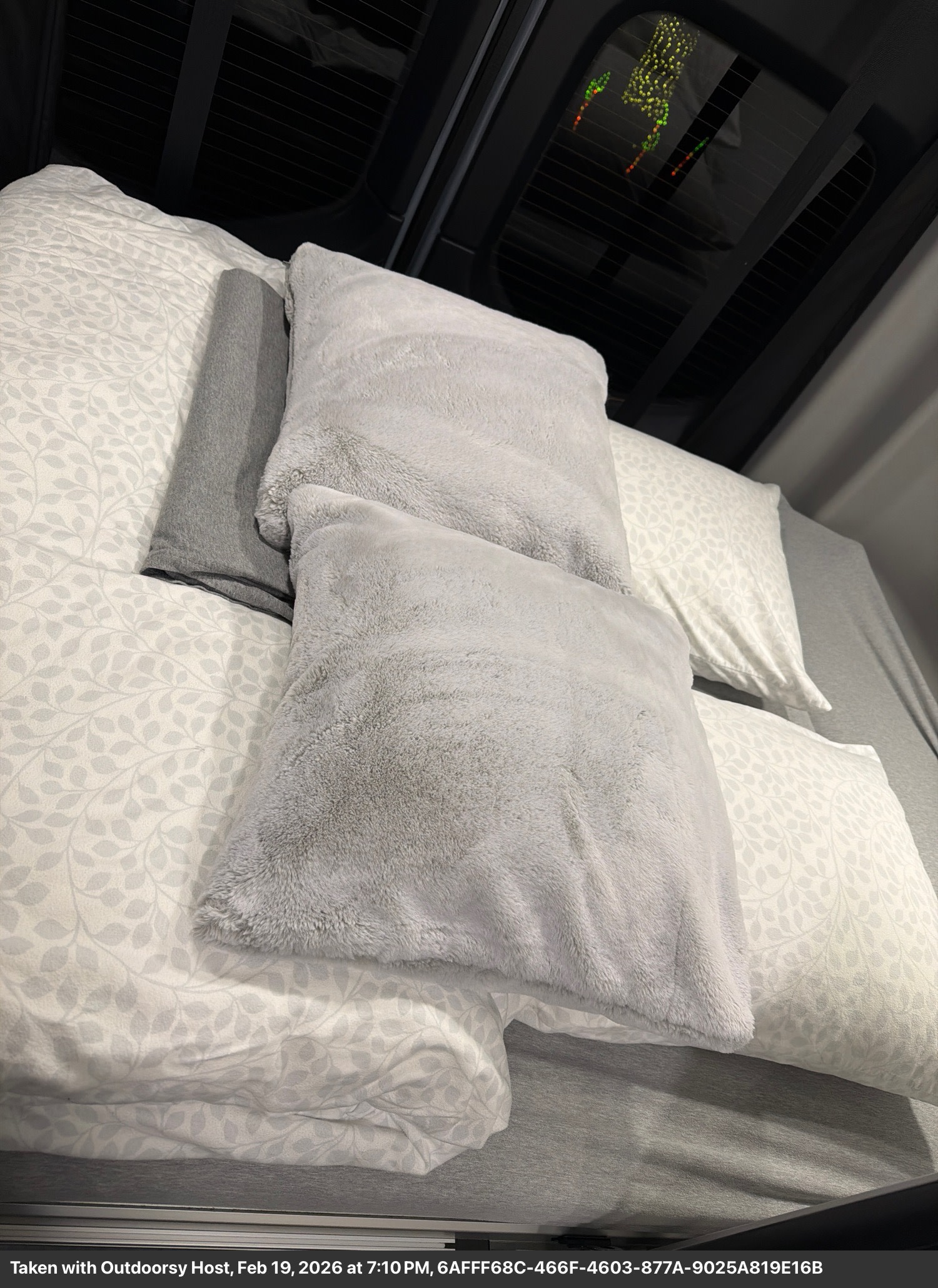 Cozy RV rental bed featuring soft gray and patterned white pillows on sheets with a leaf design, perfect for comfort.. Winnebago Revel 2025