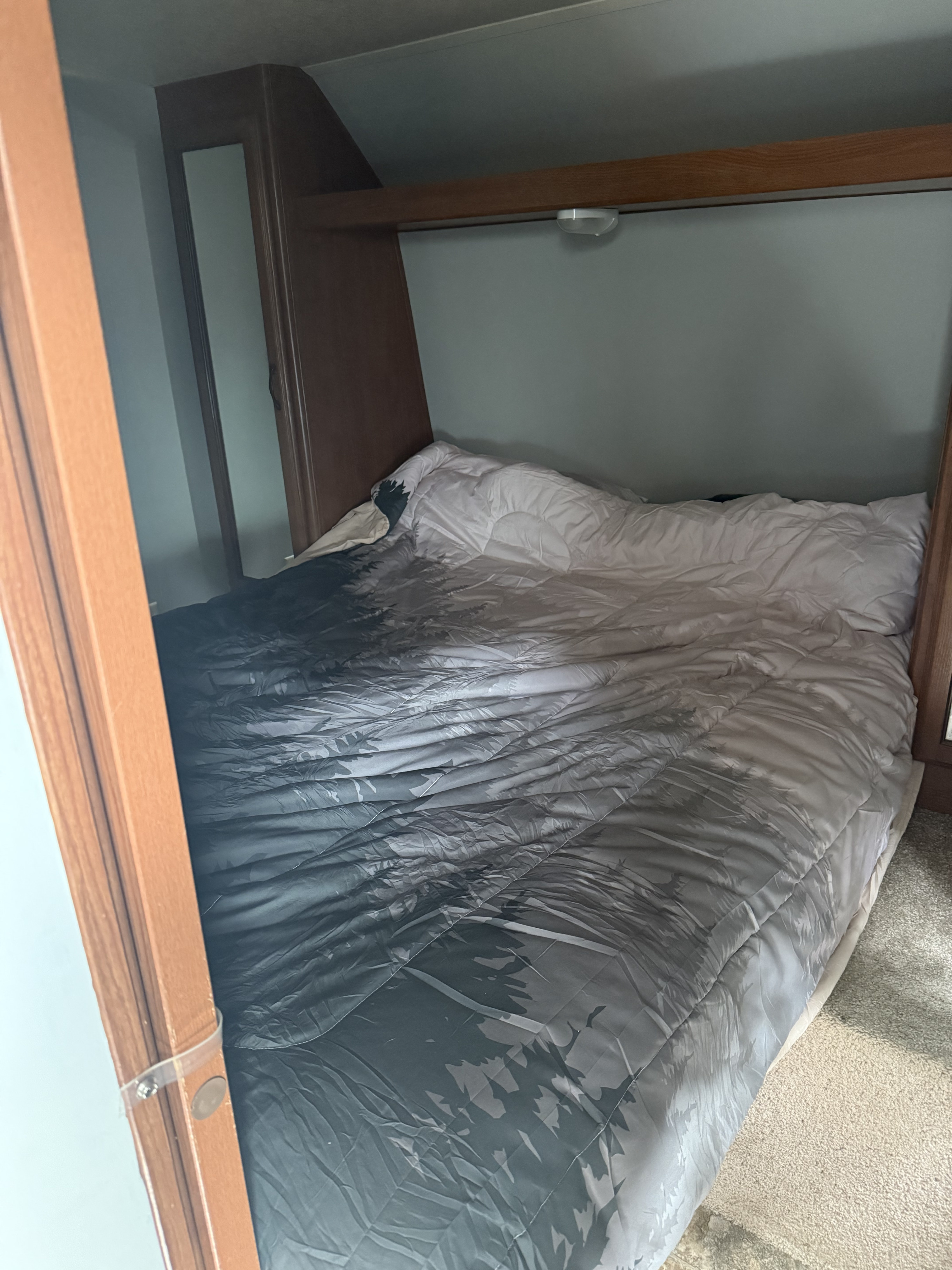 RV rental bedroom with a rumpled bed, patterned comforter, overhead light, and warm wooden interior accents.. Forest River Salem Cruise Lite 2013
