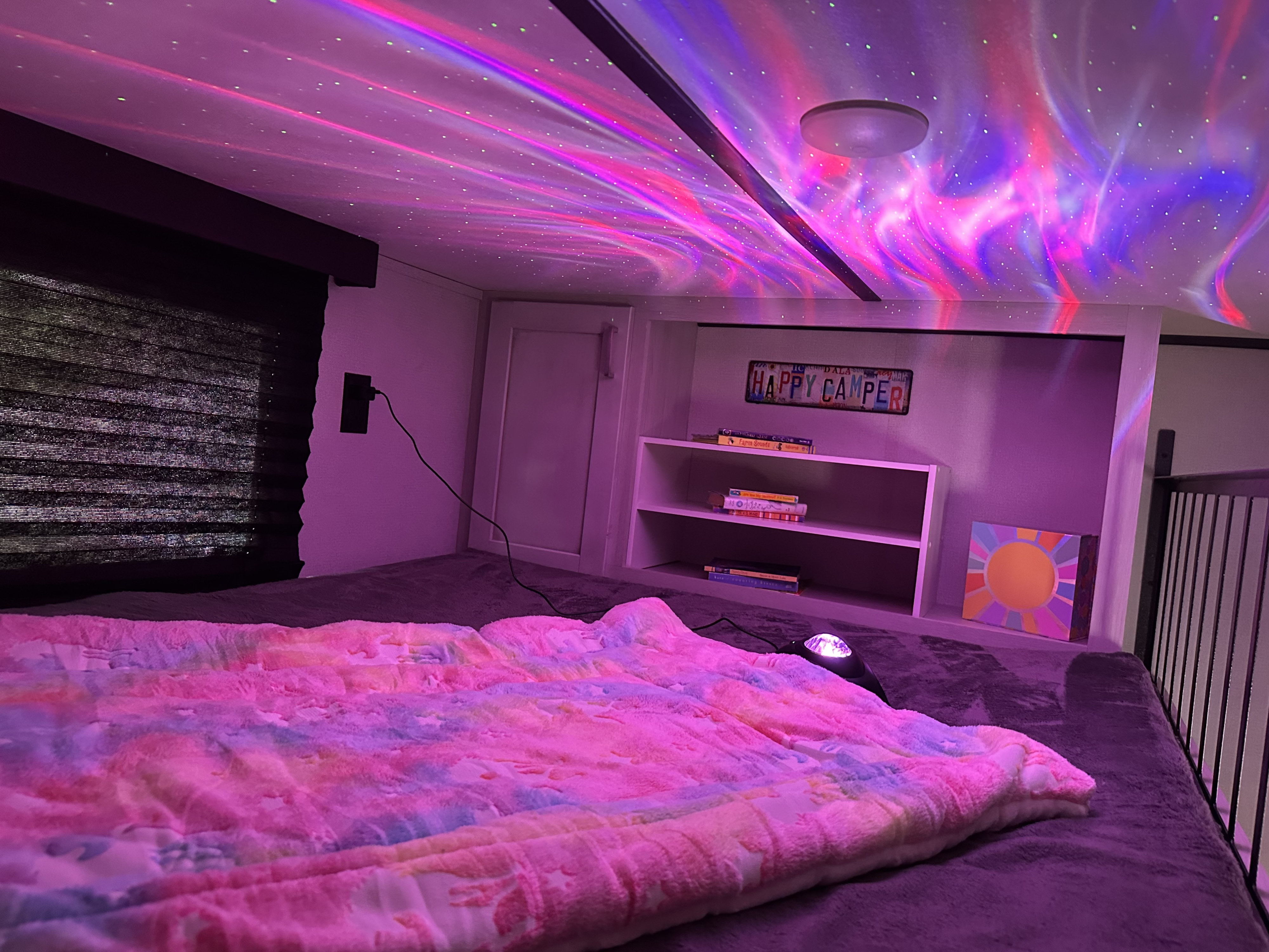 Cozy RV rental loft with starry aurora ceiling lights, a tie-dye blanket, and a 'Happy Camper' sign.. Keystone RV Sprinter 2022