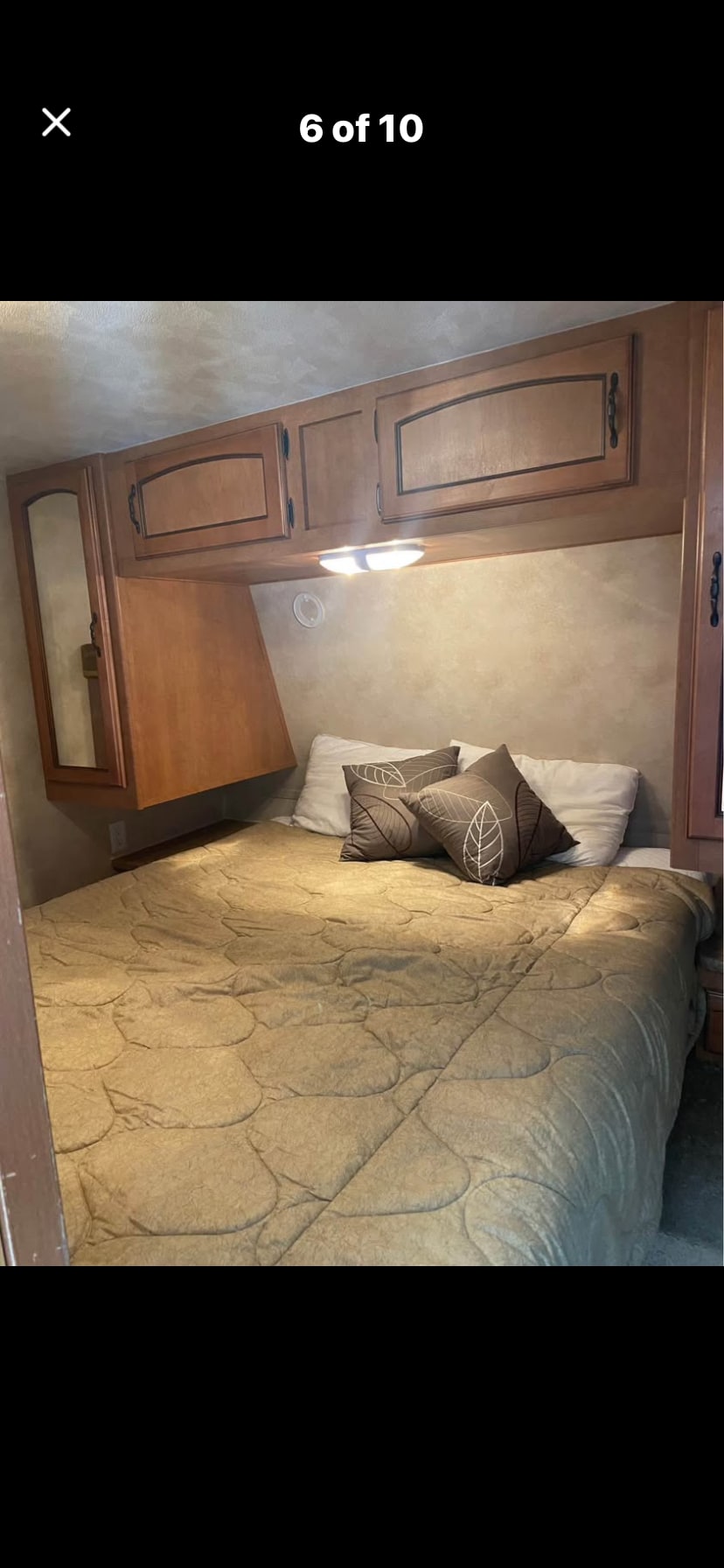 Comfortable RV rental bedroom featuring a cozy bed with patterned pillows, overhead storage, and a bedside light fixture.. Puma Puma 2011