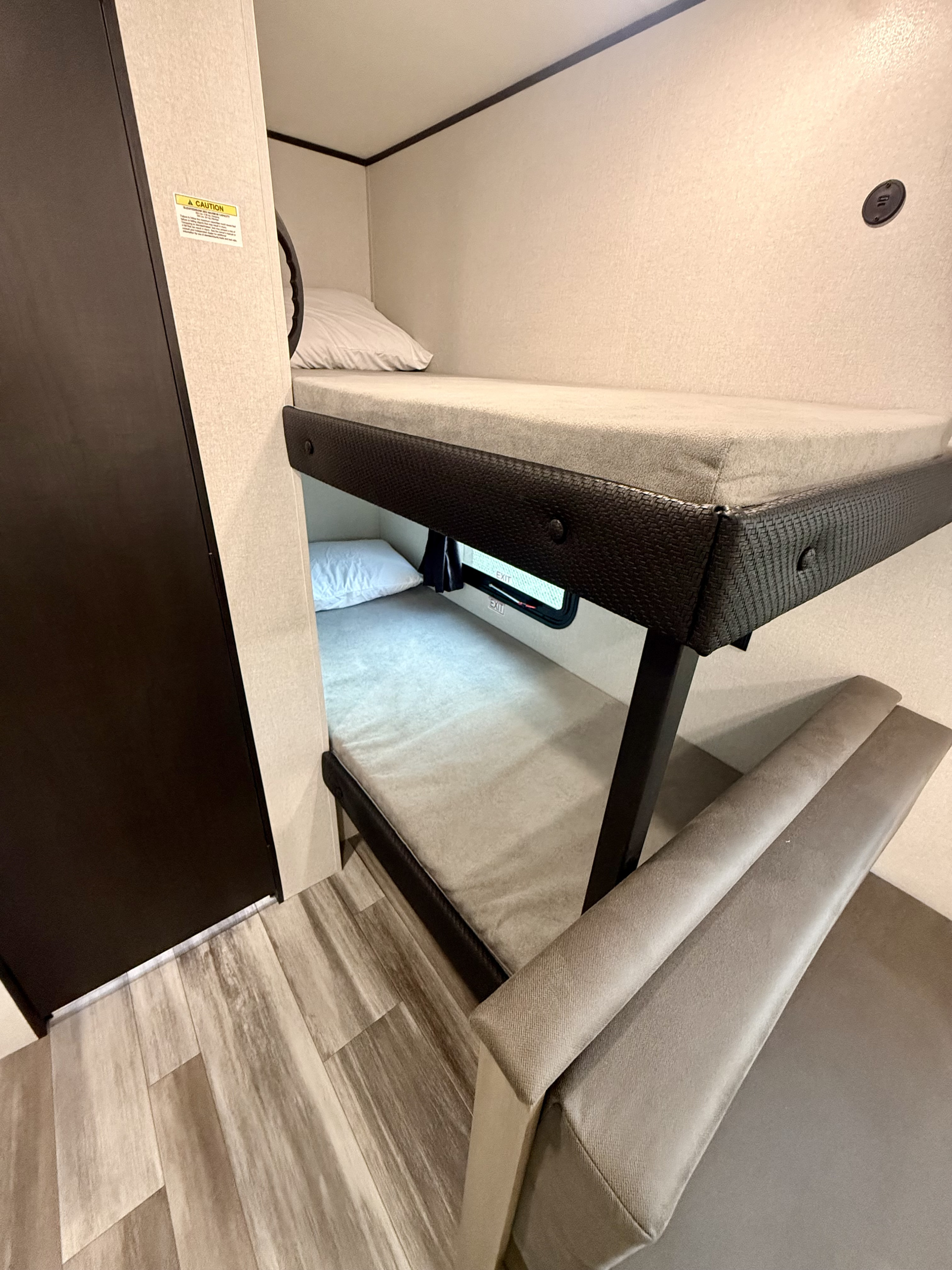 An RV rental interior features compact bunk beds with light gray mattresses, a dark brown cabinet, and plush bench seating on wood-look floors.. Jayco SLX 175BH 2026