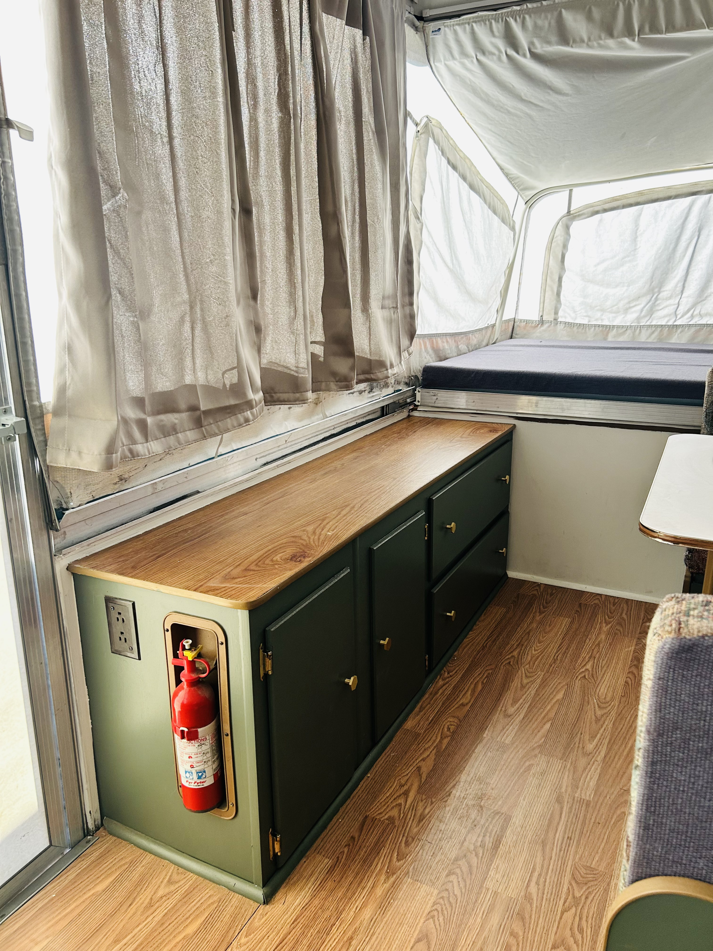 This rv rental showcases custom dark green storage cabinets with a wood top, a bed, and a fire extinguisher, offering functional comfort.. Coleman Destiny Santa Fe 1996