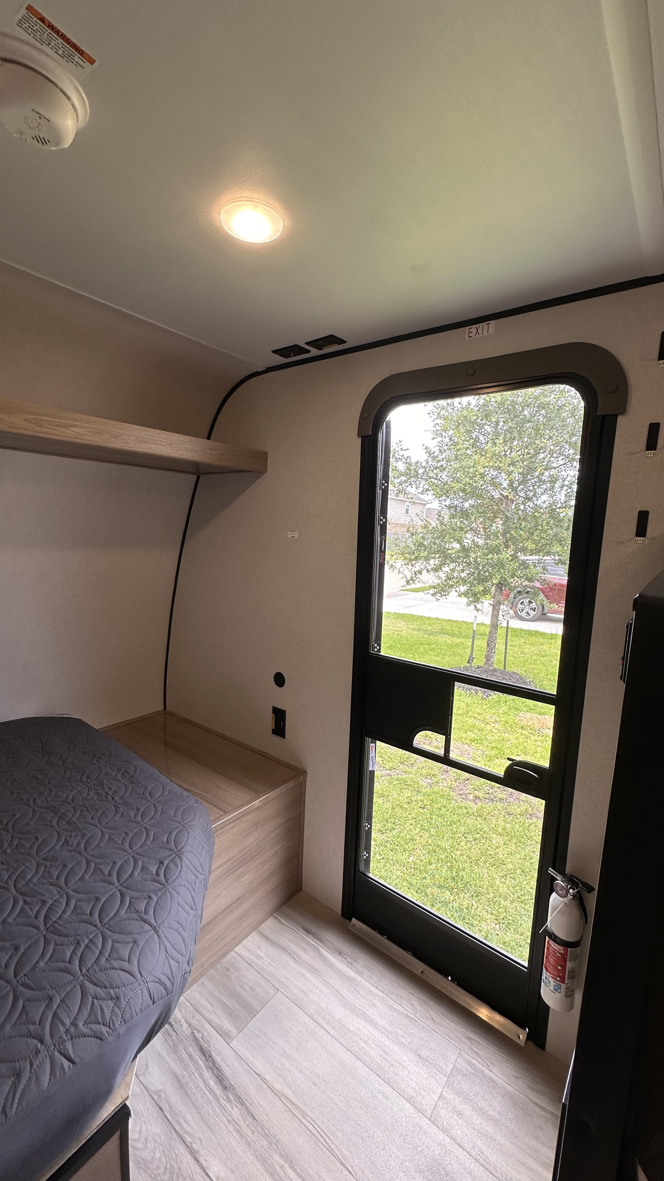 Cozy rv rental interior with a bed, shelf, ceiling light, smoke detector, and exit door with a fire extinguisher.. Keystone RV 13B travel Trailer 2026