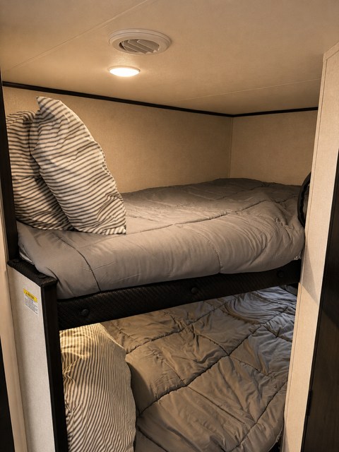 Cozy rv rental bunk beds, neatly made with gray bedding & striped pillows, featuring overhead & under-bunk lighting.. Jayco 245BHS 2026