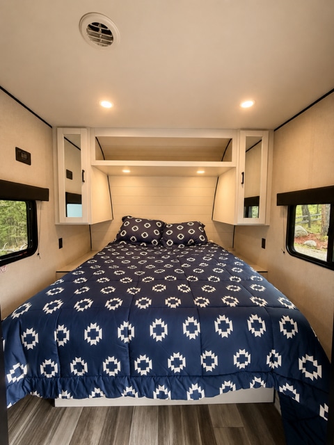 Cozy RV rental bedroom featuring a queen bed with a blue and white patterned comforter, overhead storage, and windows.. Jayco 245BHS 2026