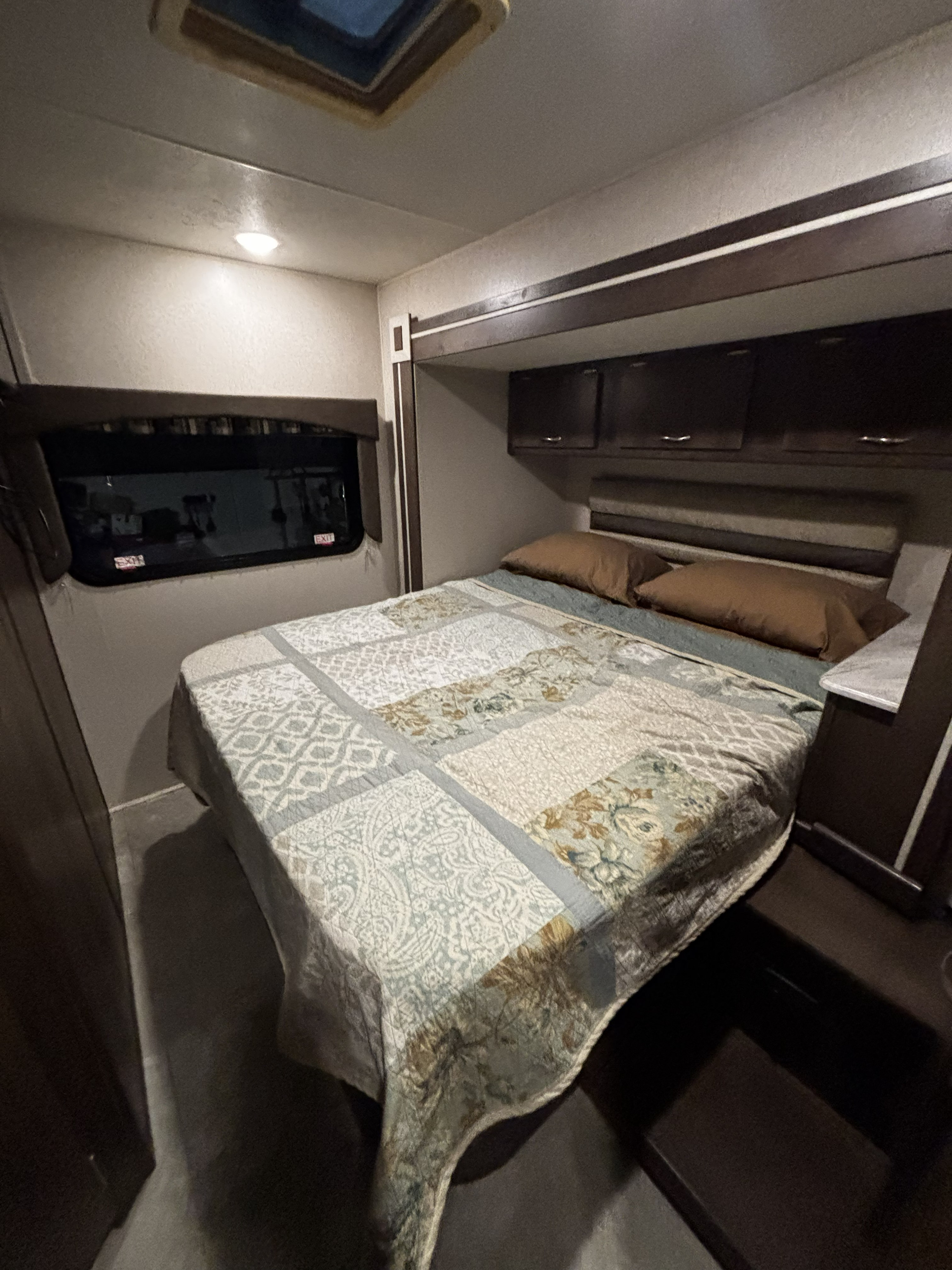 Cozy RV rental bedroom featuring a comfortable bed with a decorative quilt, overhead storage cabinets, and an emergency exit window.. Forest River Coachmen Orion 2019