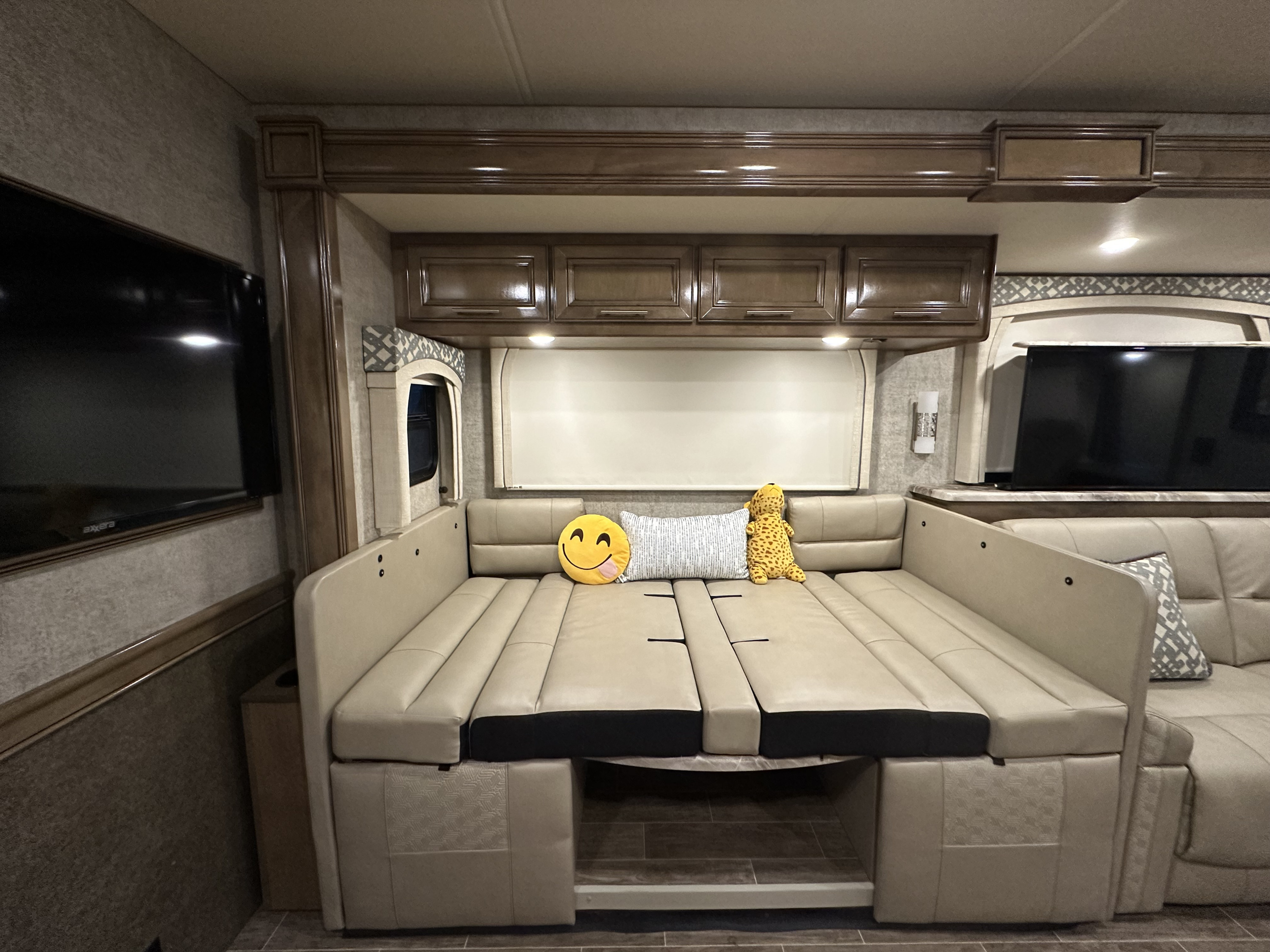 Cozy RV rental dinette converted to a bed with tan upholstery and plush toys, ideal for travel comfort.. Thor Miramar 2020