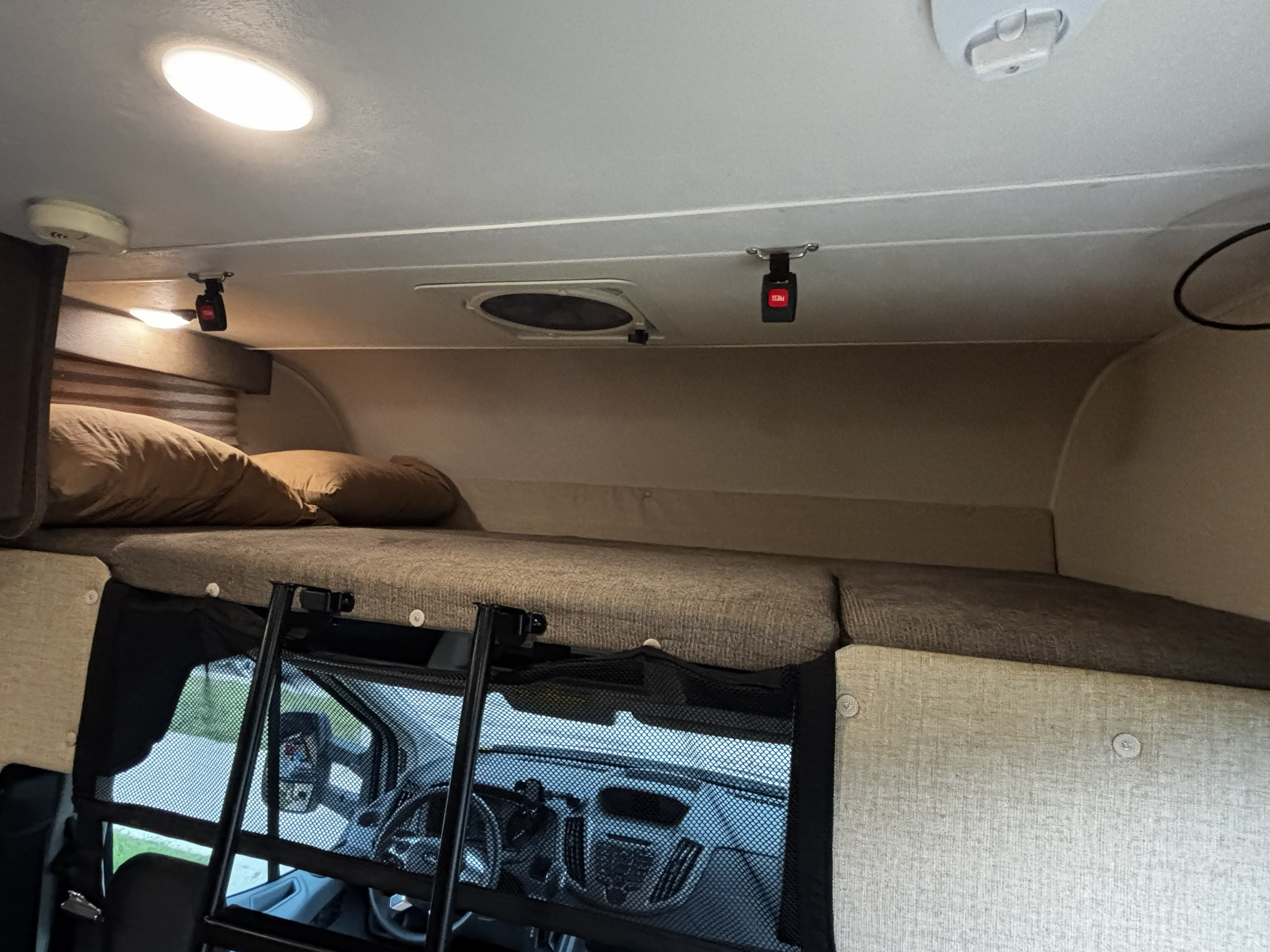 This RV rental features a cozy overhead bunk bed with pillows, a safety net, and a ladder, overlooking the vehicle's cab.. Forest River Coachmen Orion 2019