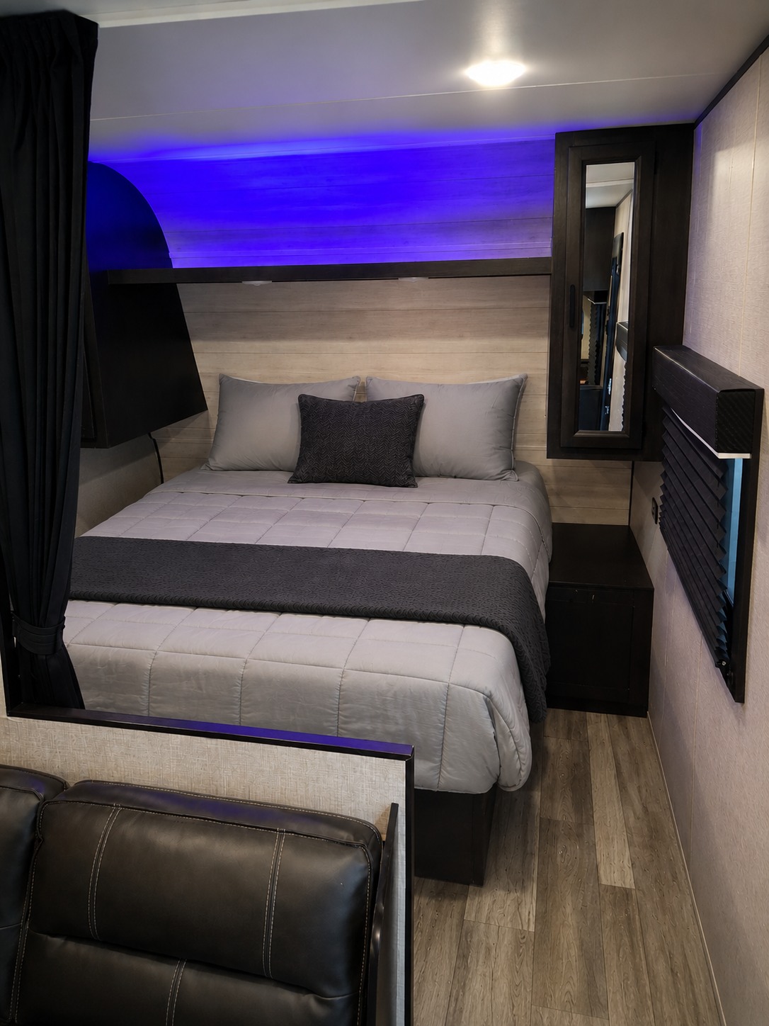 Cozy RV rental bedroom with a gray bed, vibrant blue accent lighting, dark curtains, and a mirror. Ideal for your next adventure.. Jayco Jay Flight SLX Rocky Mountain Edition 2022