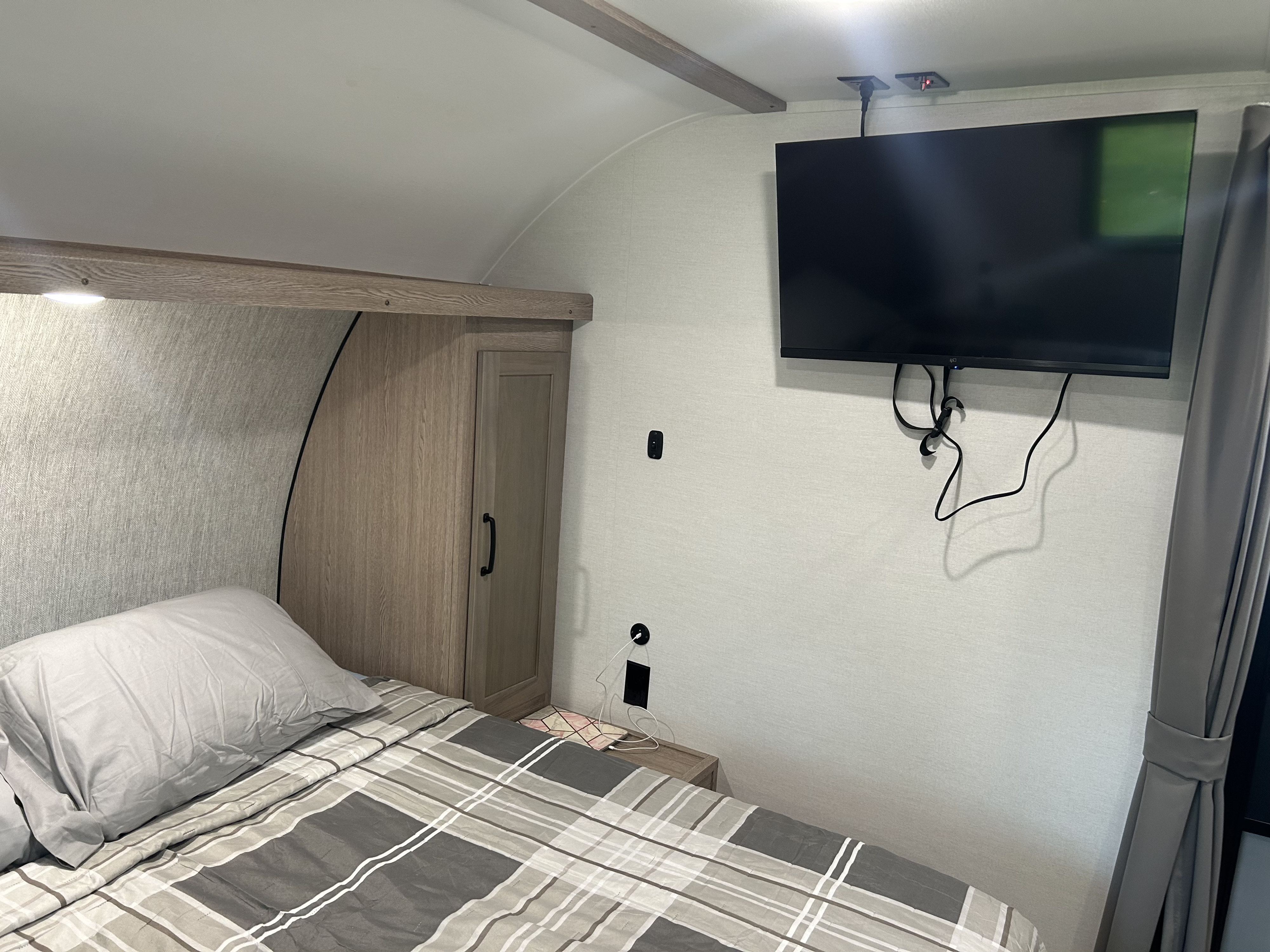 Cozy rv rental bedroom with a mounted TV, comfortable bed, and compact storage, ideal for travel.. Gulf Stream Grand River 25BH 2026