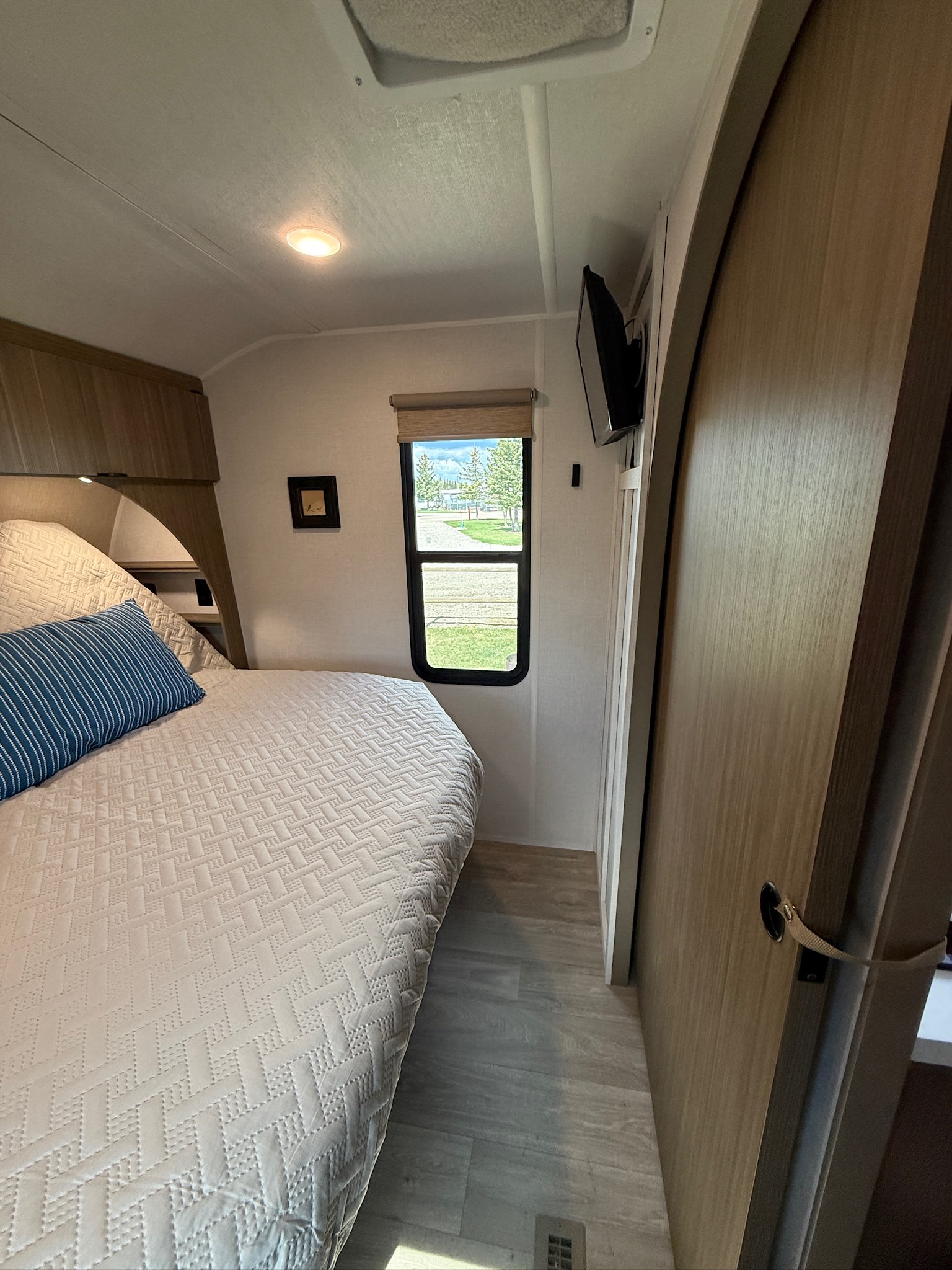 This inviting RV rental bedroom features a comfortable bed, window with a scenic view, wall-mounted TV, and wooden accents.. Forest River Wildwood 260ICE 2026