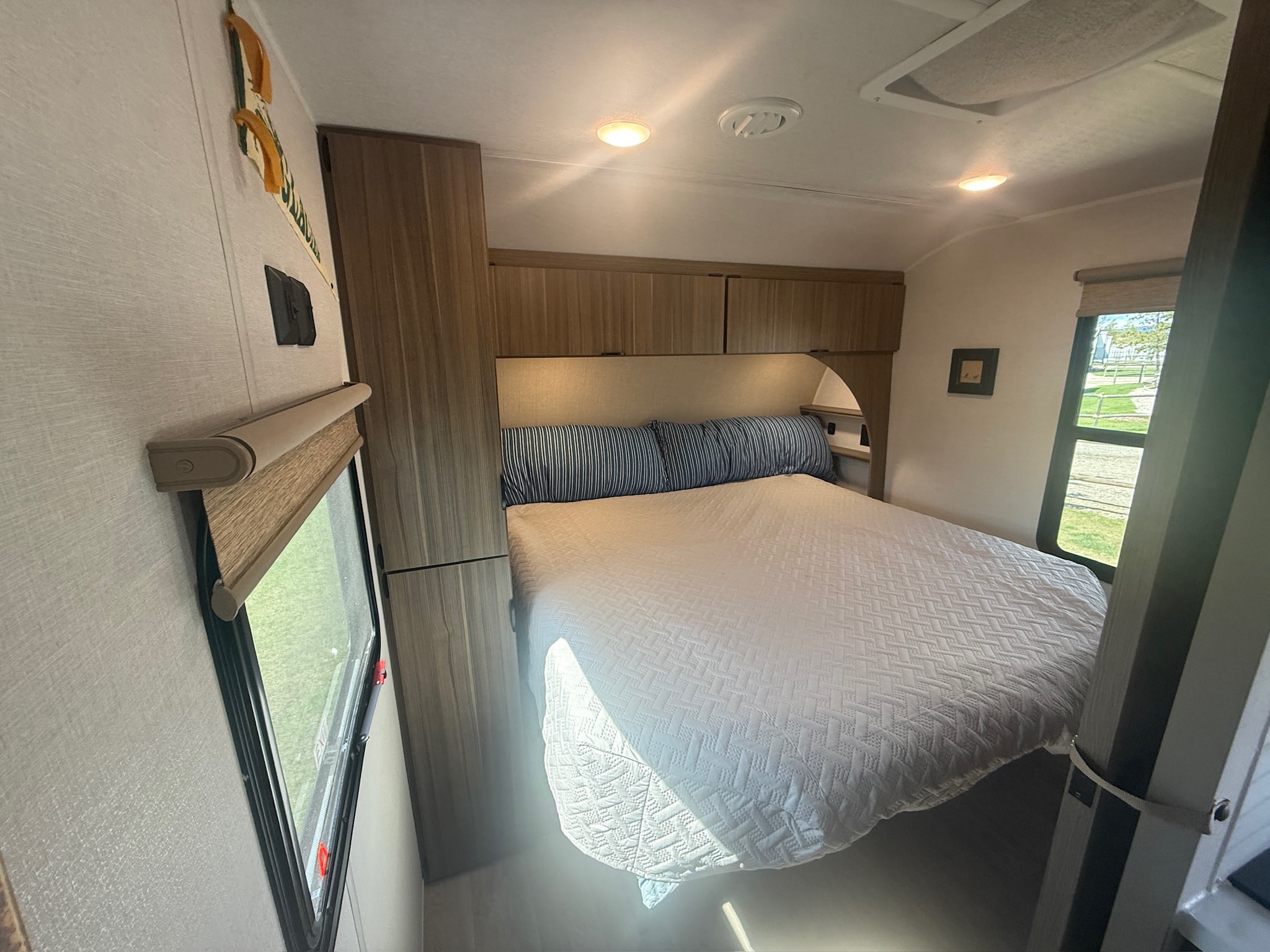 Bright RV rental bedroom: cozy bed, overhead cabinets, and window with outdoor views.. Forest River Wildwood 260ICE 2026