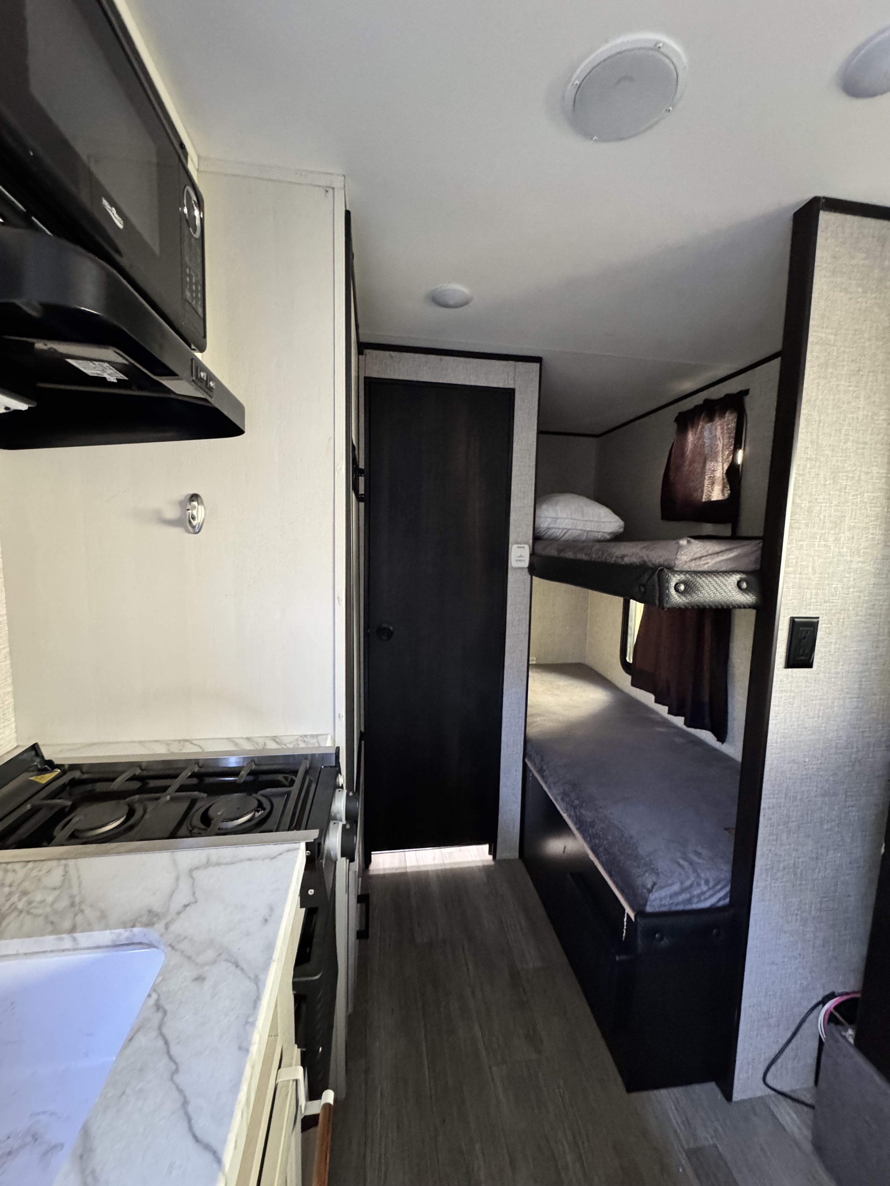 RV rental interior with a kitchen (stove, sink, microwave) on the left and bunk beds on the right, offering compact living.. Jayco Jay Flight SLX Baja Edition 2022