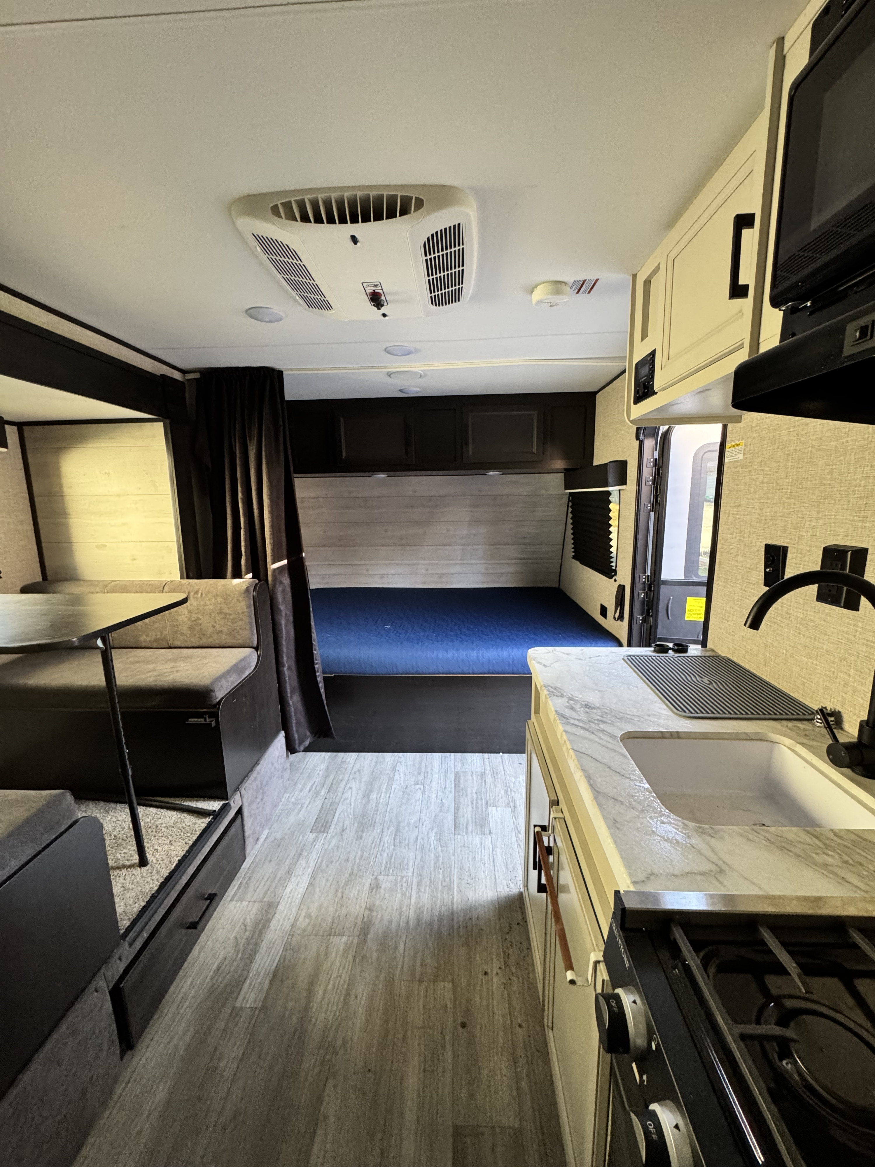 Interior of an rv rental, showing the kitchen, dinette seating, and a bunk bed with blue mattress. Light-toned flooring.. Jayco Jay Flight SLX Baja Edition 2022