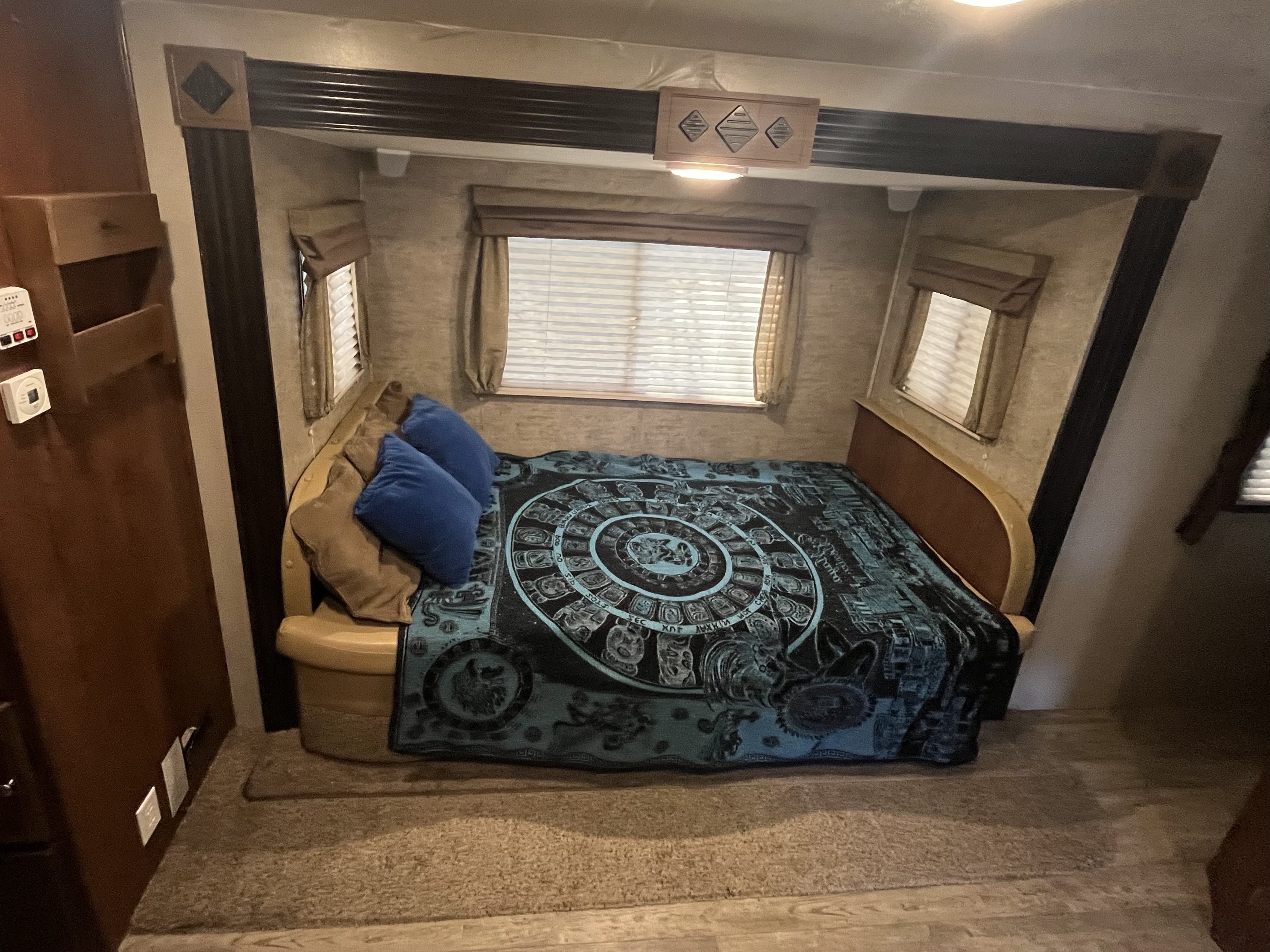 Cozy RV rental sleeping area featuring a comfortable bed with a patterned blanket, pillows, and windows. Ideal for travel trailer getaways.. Coachmen 231RBDS 2017