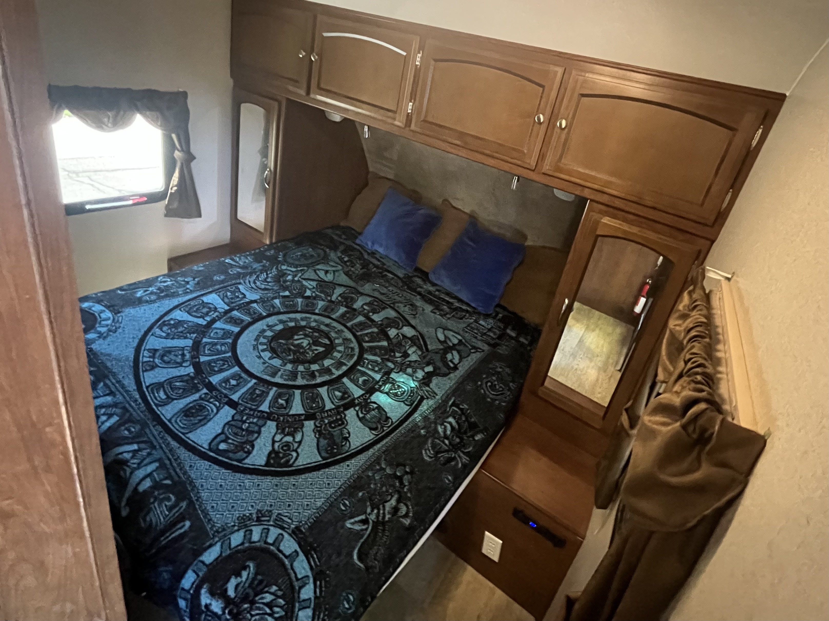 This compact rv rental bedroom features a cozy bed with a blue patterned comforter, built-in cabinets, and side mirrors.. Coachmen 231RBDS 2017