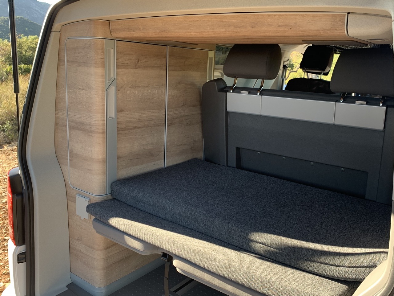 **RV rental**: Interior view of a camper van with a folded-out bed, wood-look cabinets & rear seating.. VOLKSWAGEN CALIFORNIA 2023