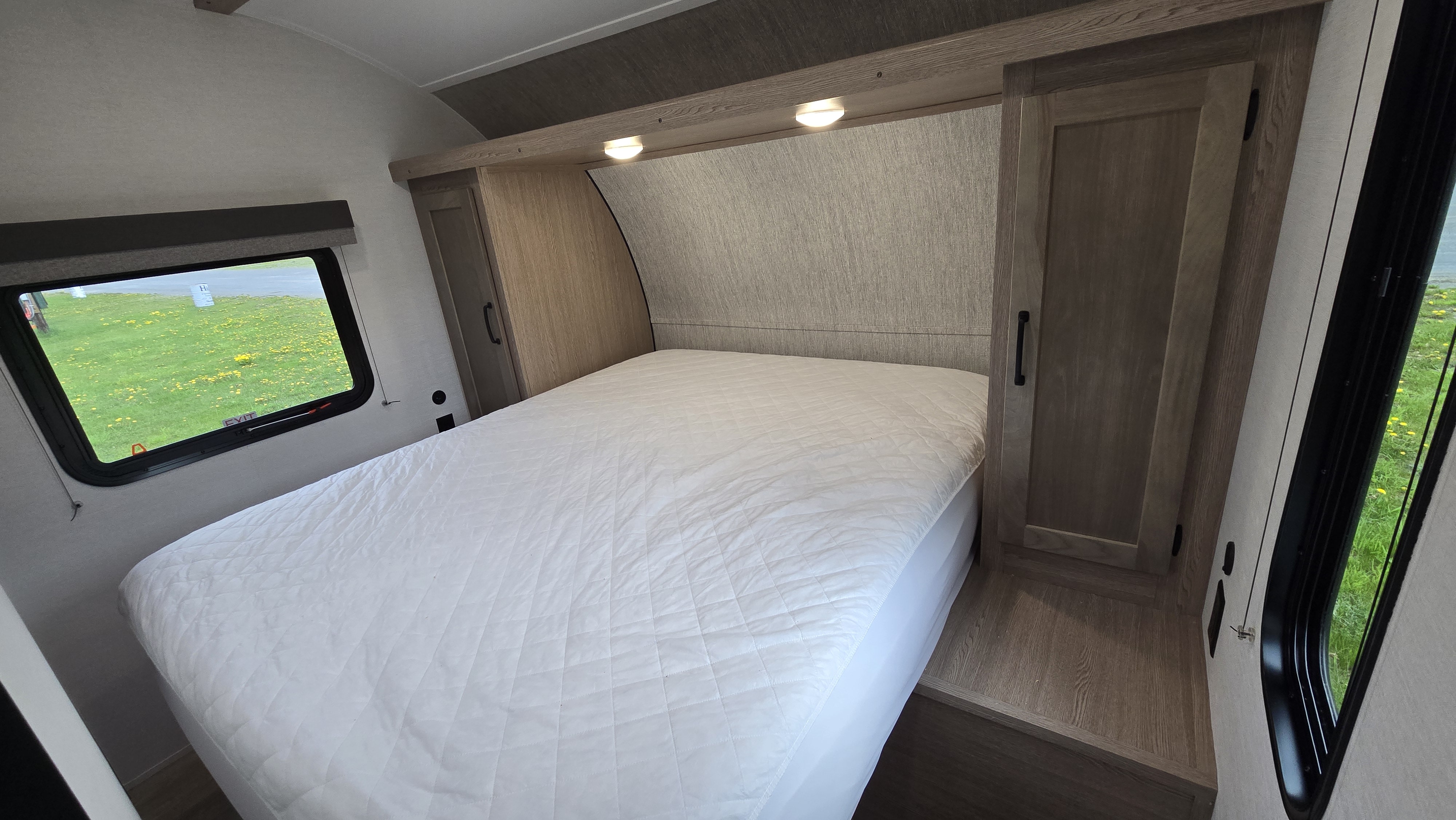 RV rental bedroom featuring a comfy bed with quilted mattress, surrounding cabinets, and windows showing green grass.. Gulf Stream 279BH 2026