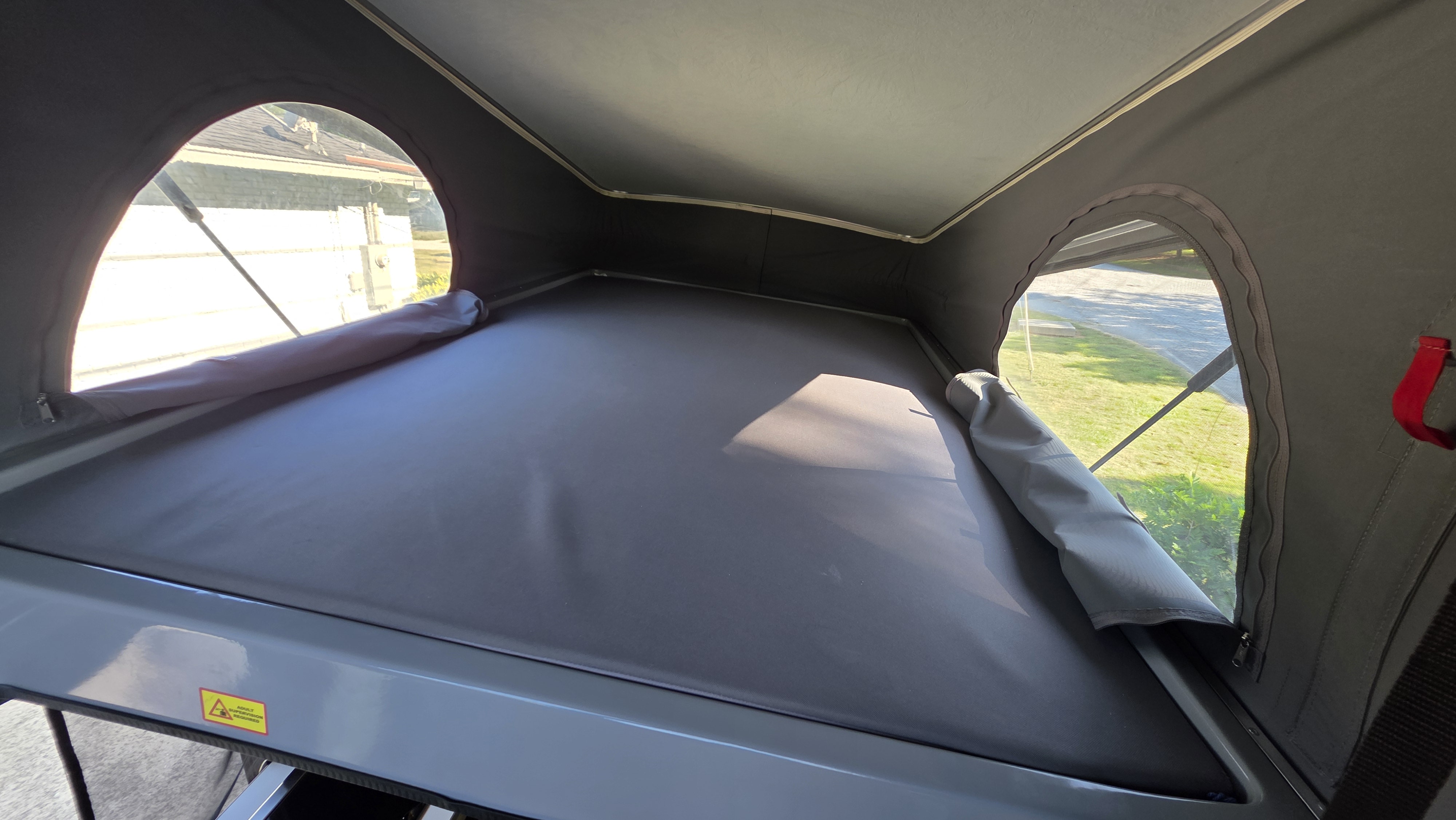 View inside an RV rental's pop-top, showing the bed and clear windows for natural light and views.. Winnebago Solis 2023
