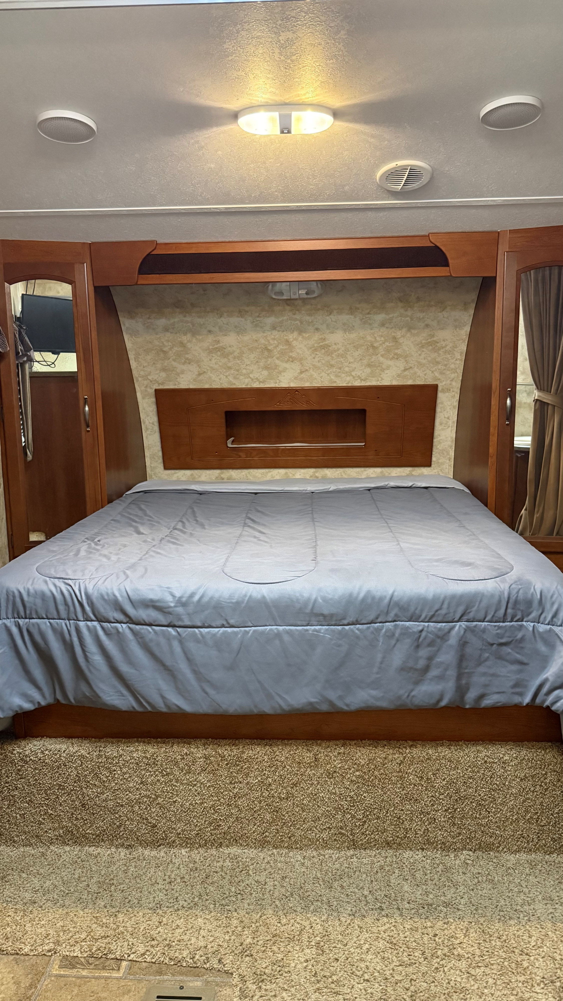 RV rental bedroom with a gray bed, wooden cabinetry, and ceiling lights/vents. A cozy, functional interior space.. Keystone RV Cougar 2012