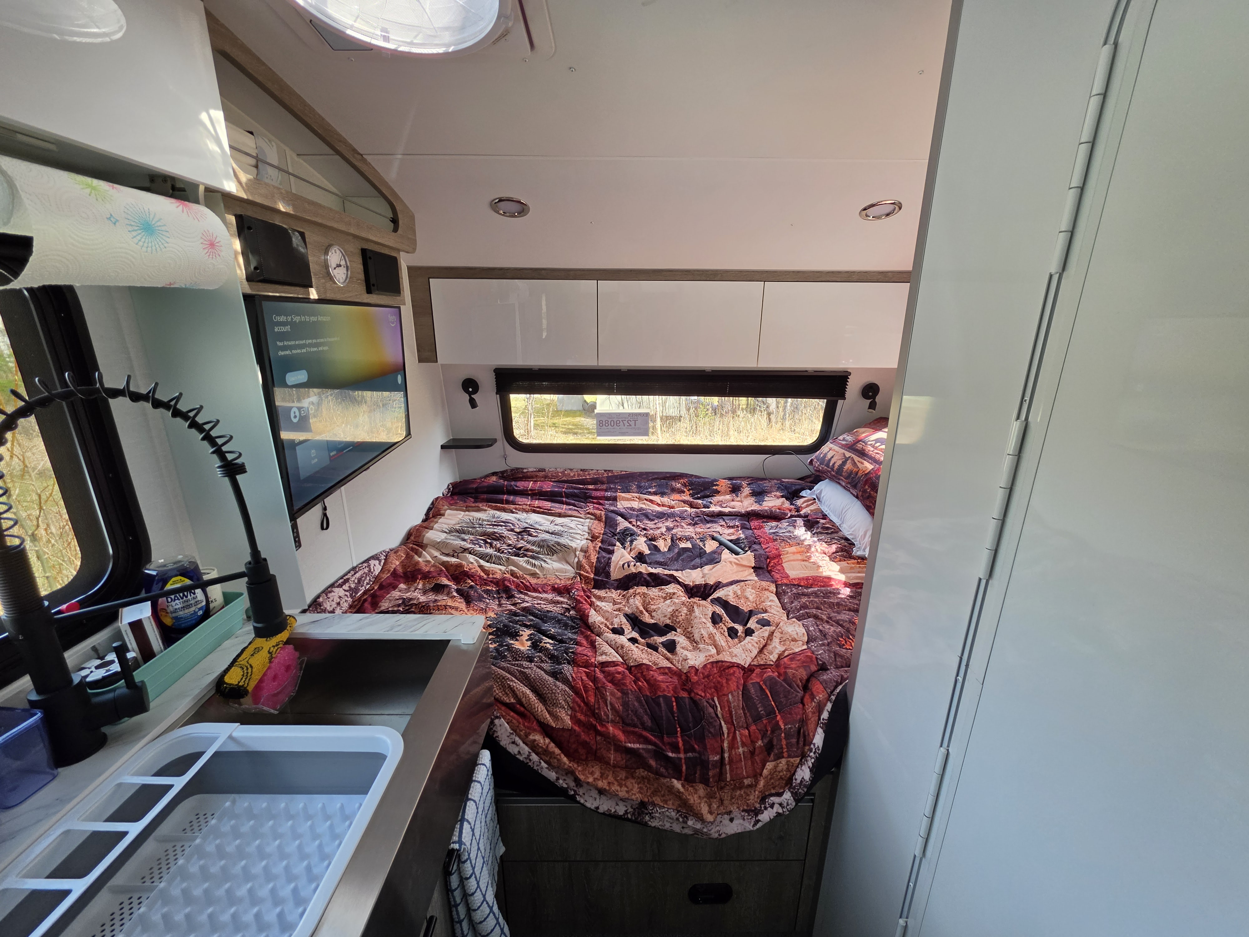 Cozy RV rental interior: bedroom with colorful comforter, TV displaying Amazon login, and compact kitchen area with sink.. InTech RV Sol 2026