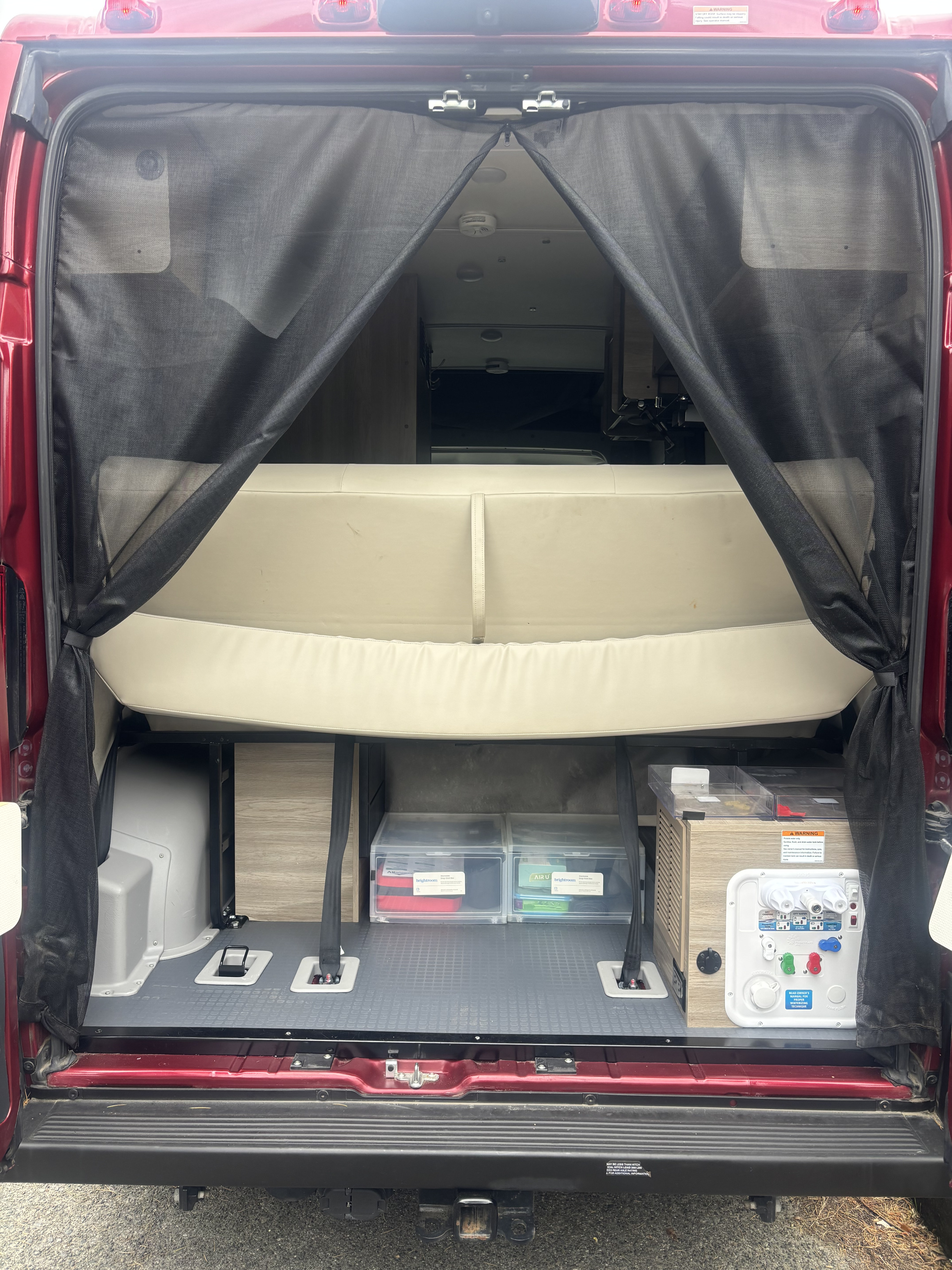 Rear interior of an RV rental with a mesh screen, revealing a bed/bench, storage, and a utility panel on a camper van.. Winnebago Solis 2022