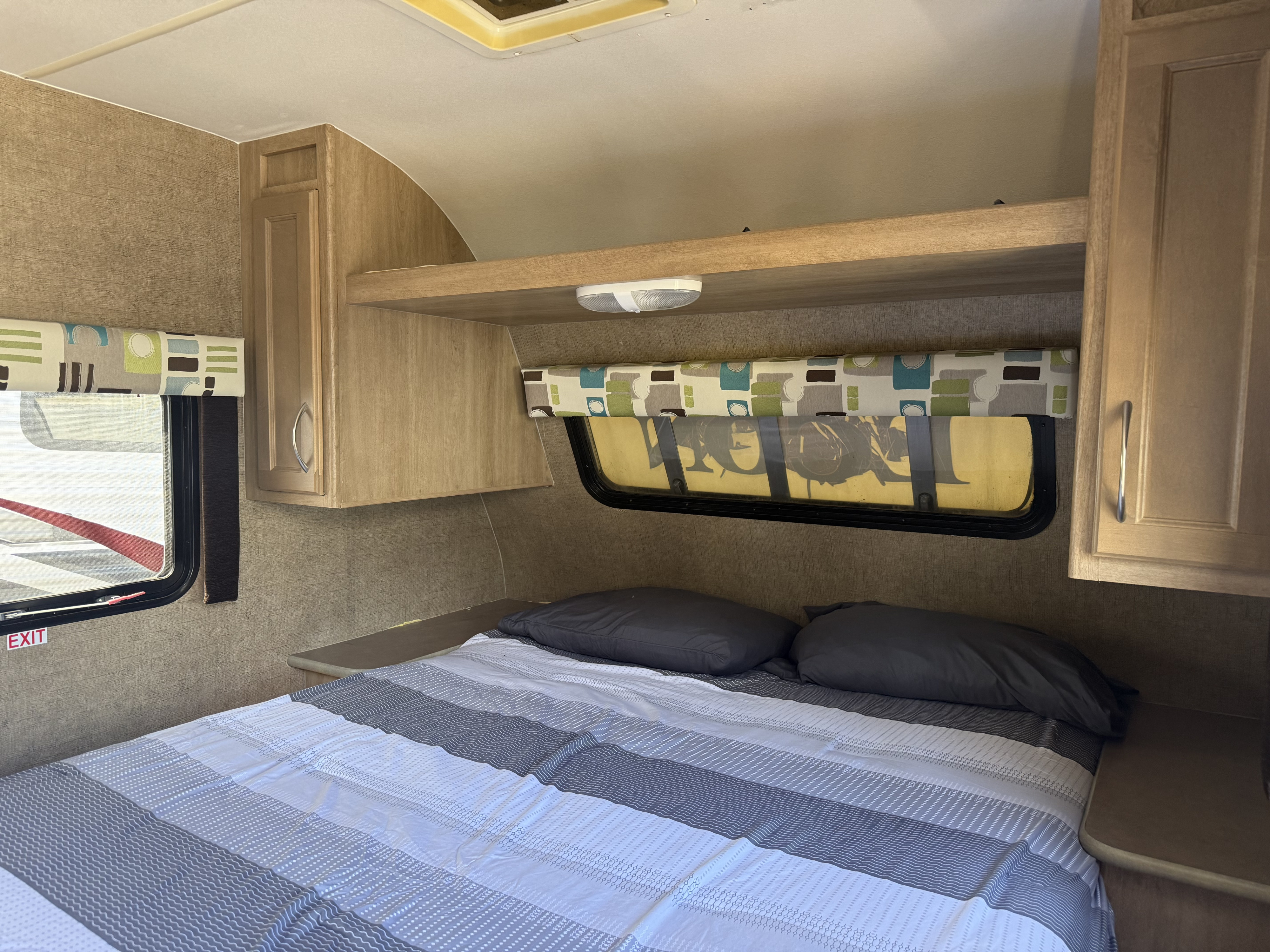RV rental interior shows a compact bedroom with striped bedding, dark pillows, wood cabinets, and a window.. Econ CCH 2016